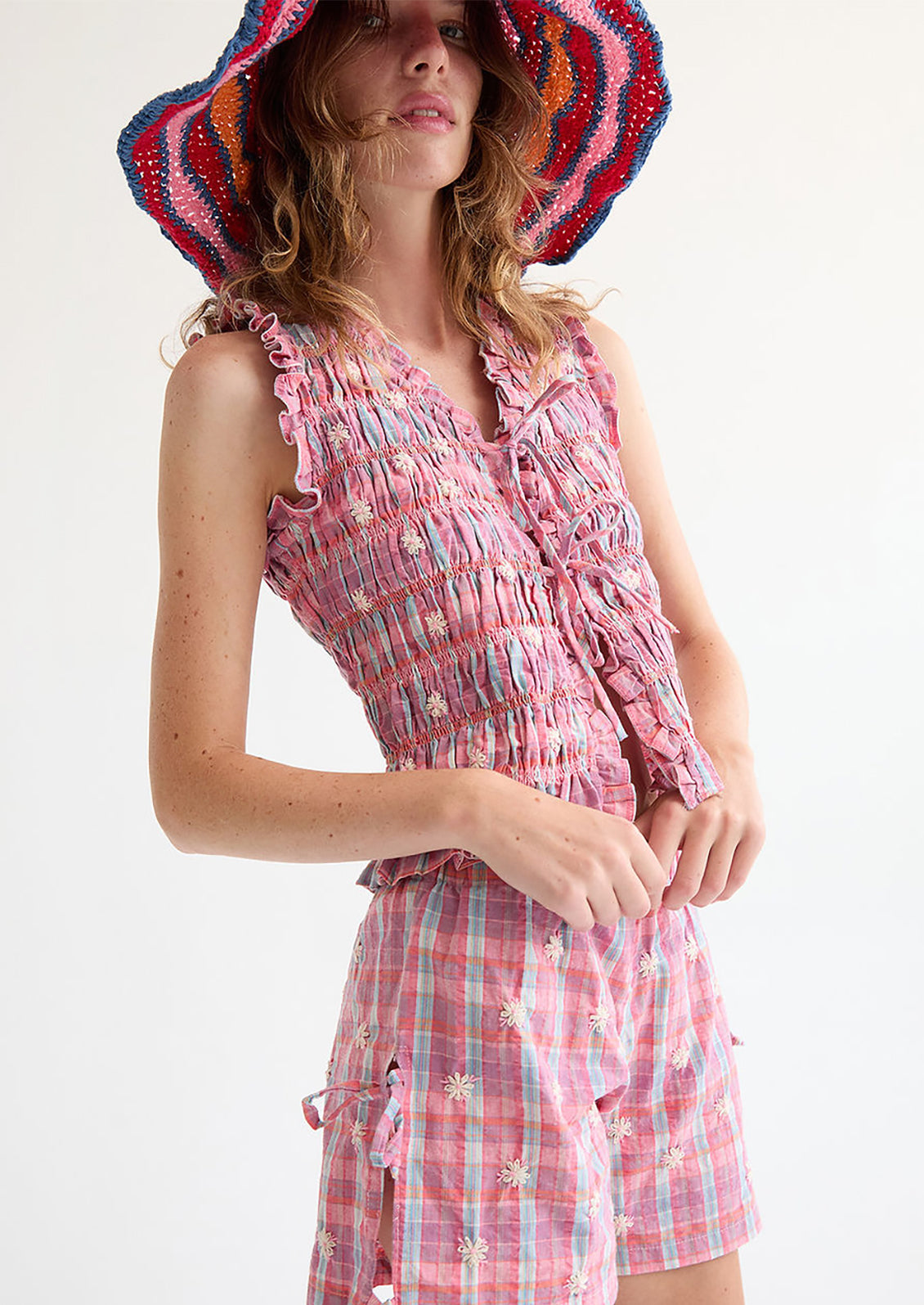 A woman wearing a smocked top in pink and blue, with tie front closure.
