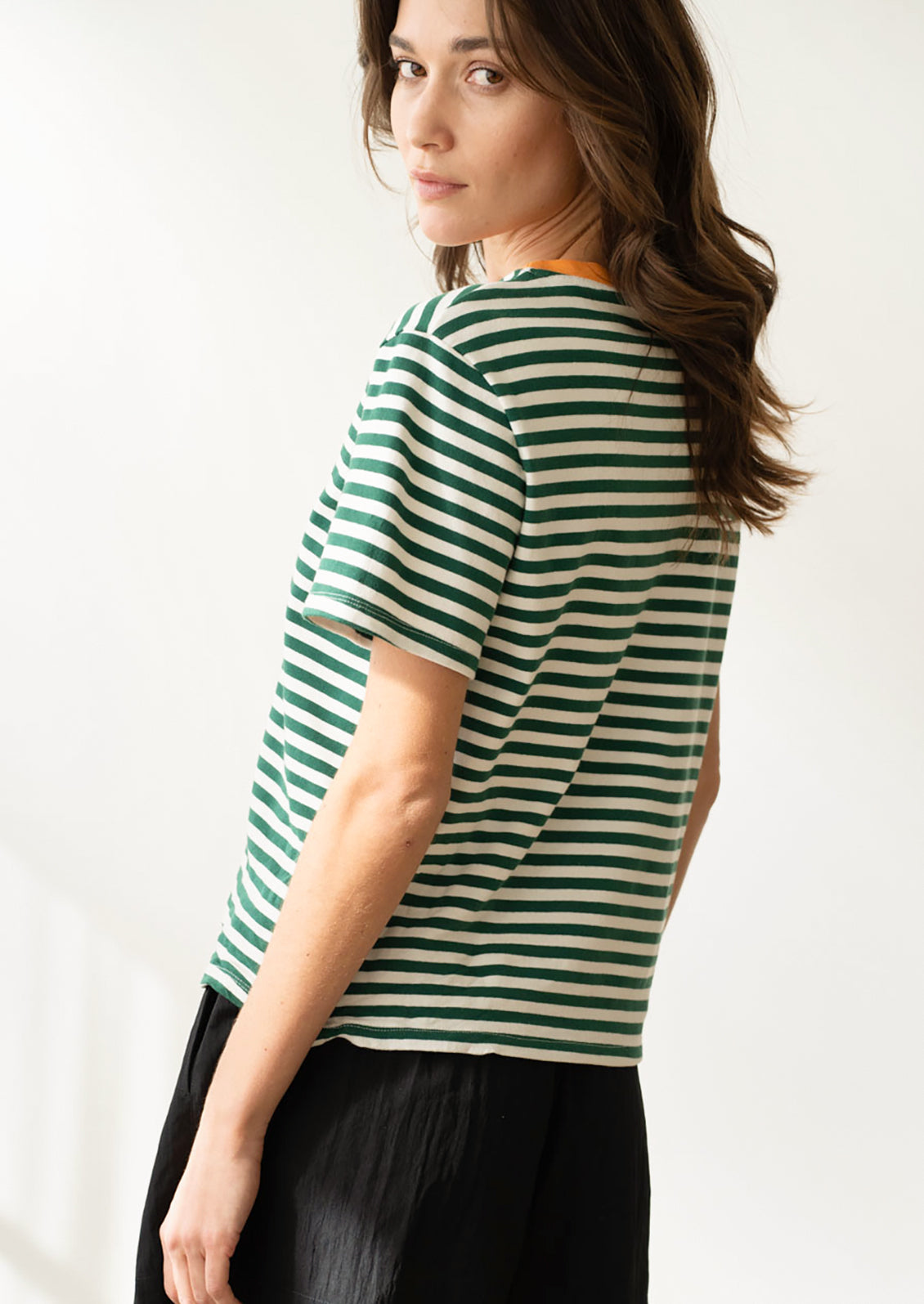 A woman wearing a short sleeve t-shirt in green and white stripes with orange neck trim.