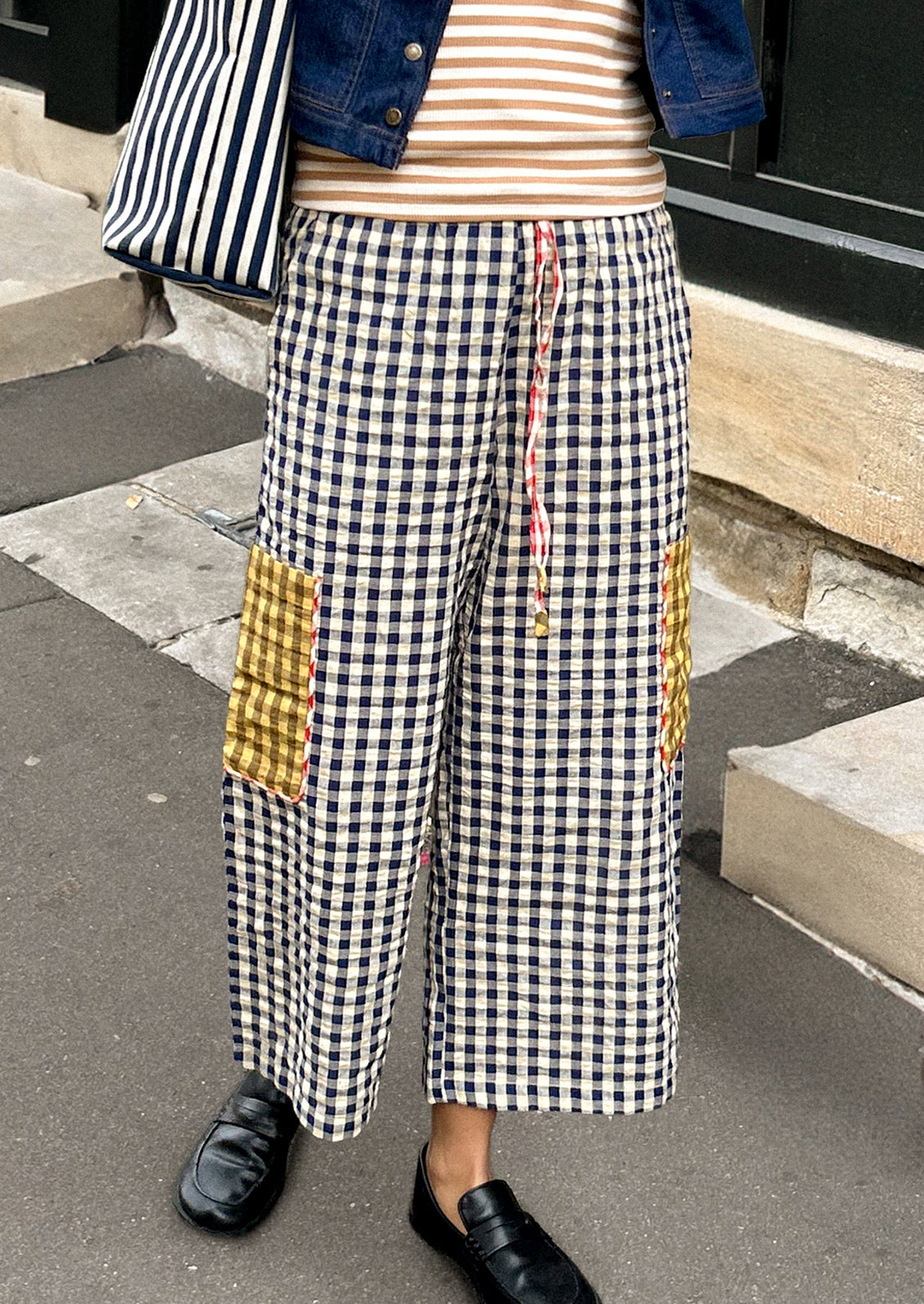 Person wearing a striped shirt, denim jacket, and checkered pants with gold accents on a city street.