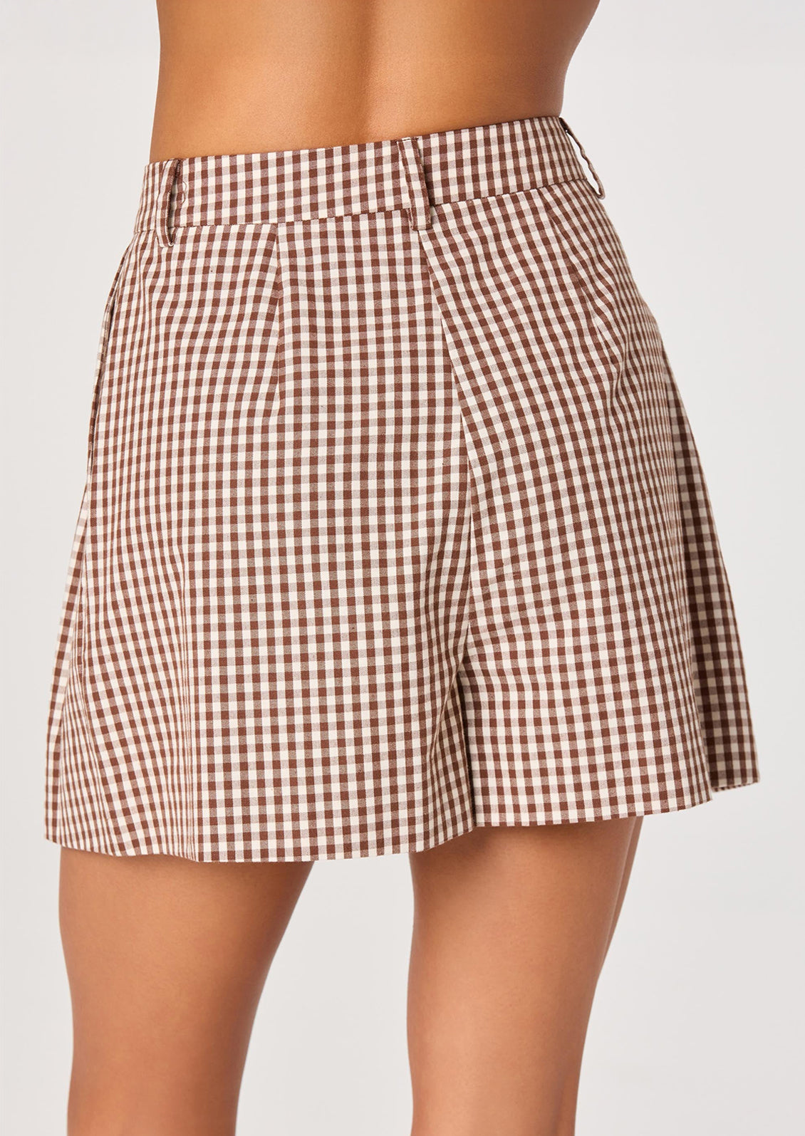 A person wearing a pair of pleated shorts in brown and white gingham.