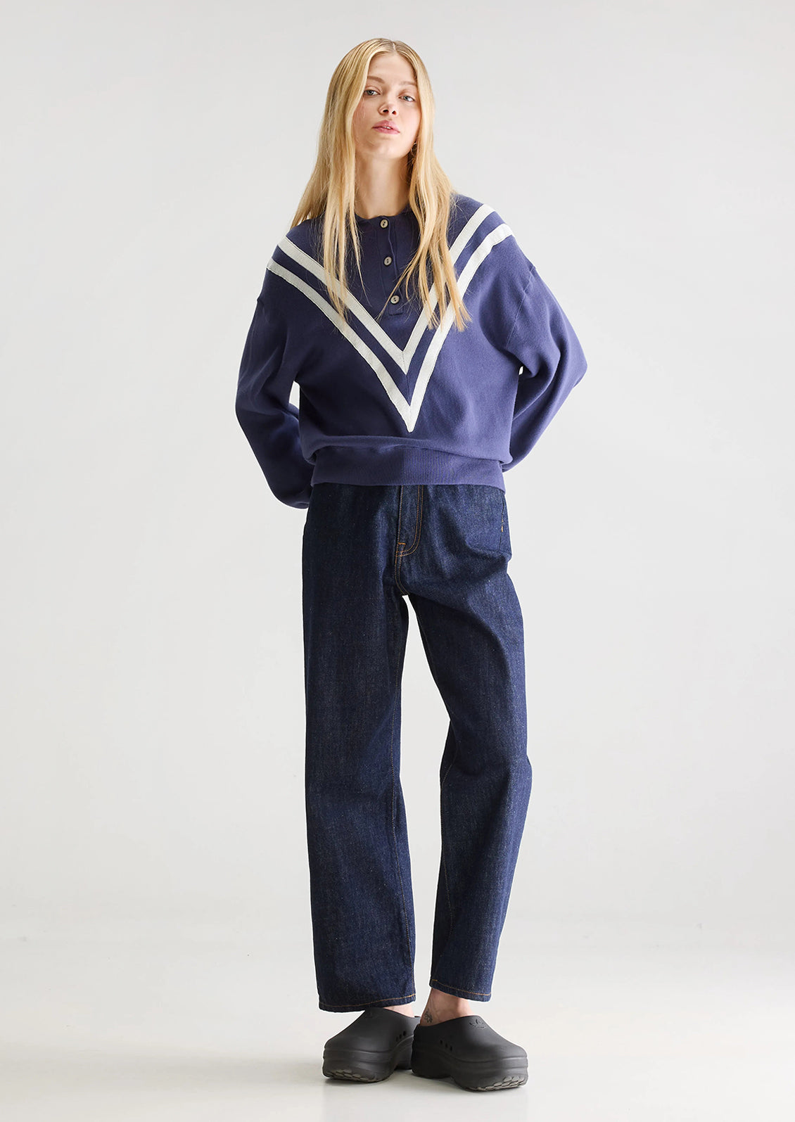 A woman wearing a navy blue henley long sleeve polo with inset V-shaped contrast detailing.