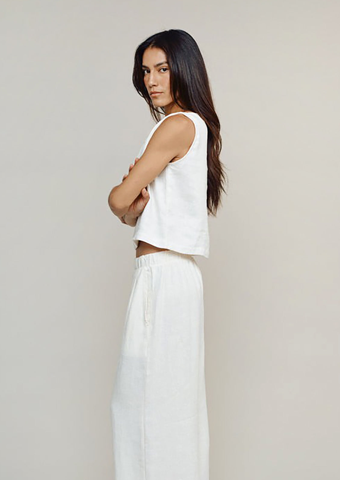 Woman wearing a white sleeveless top and pants against a plain background