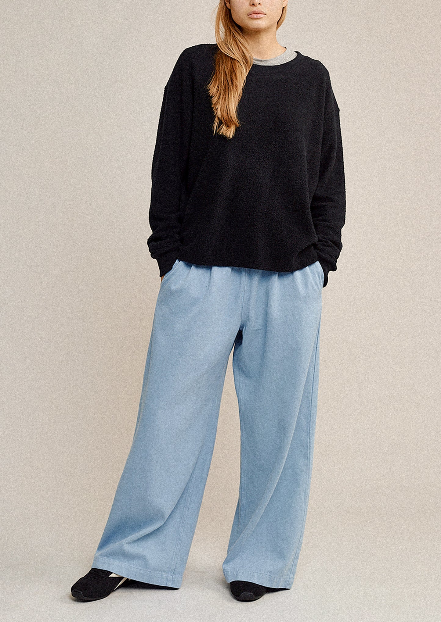 Person wearing a black sweater and light blue pants on a beige background