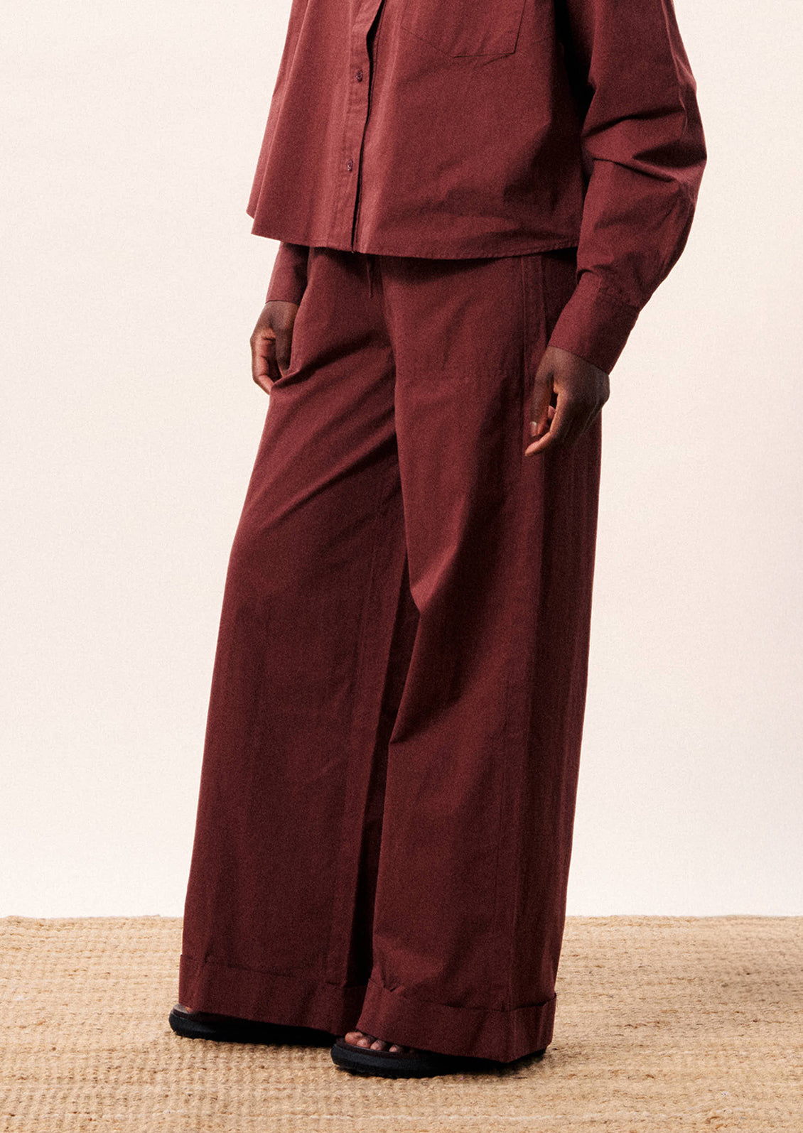 A person wearing a pair of wide leg cotton pants in wine color.