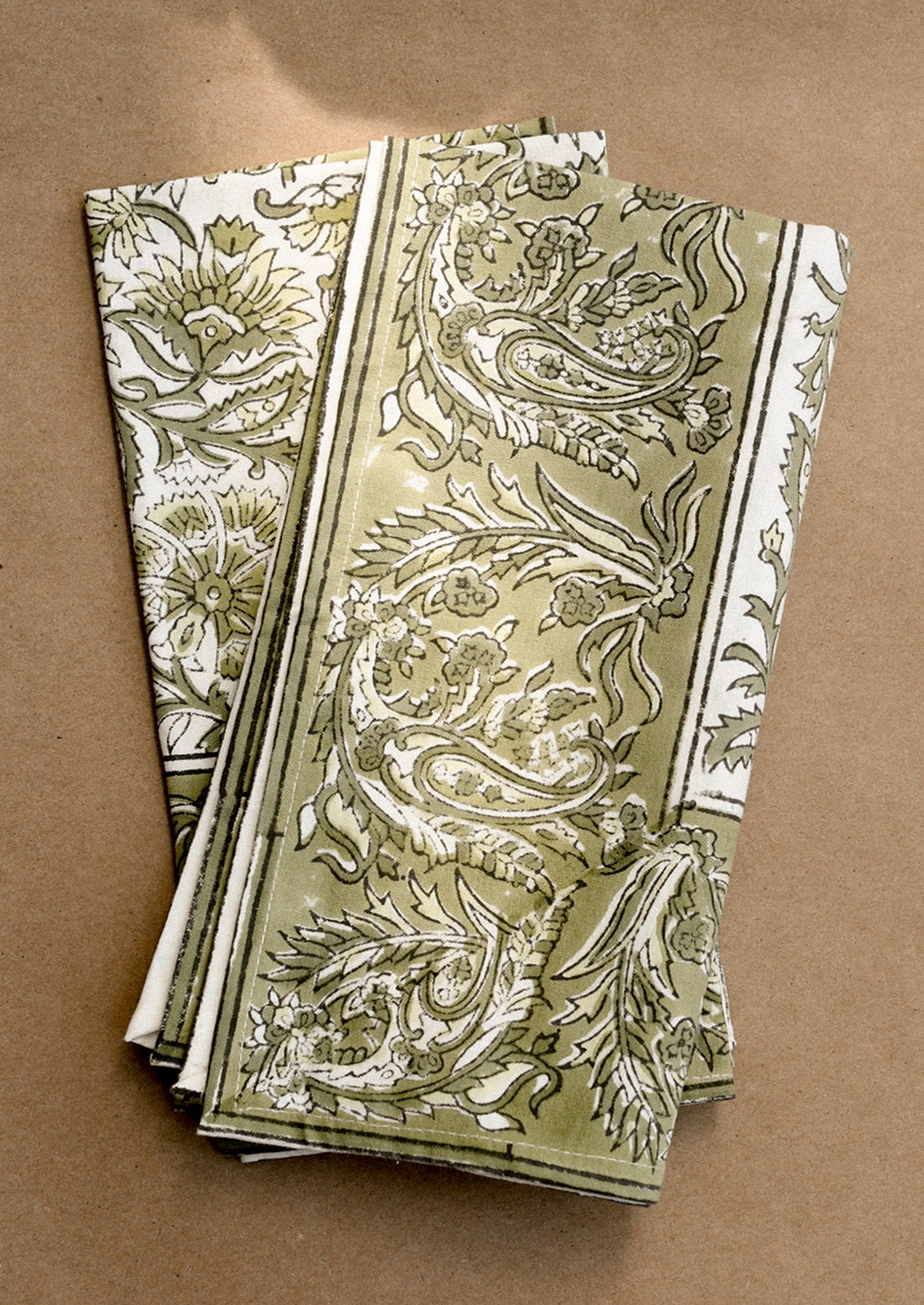 A set of cloth napkins in green and white traditional floral block print pattern.