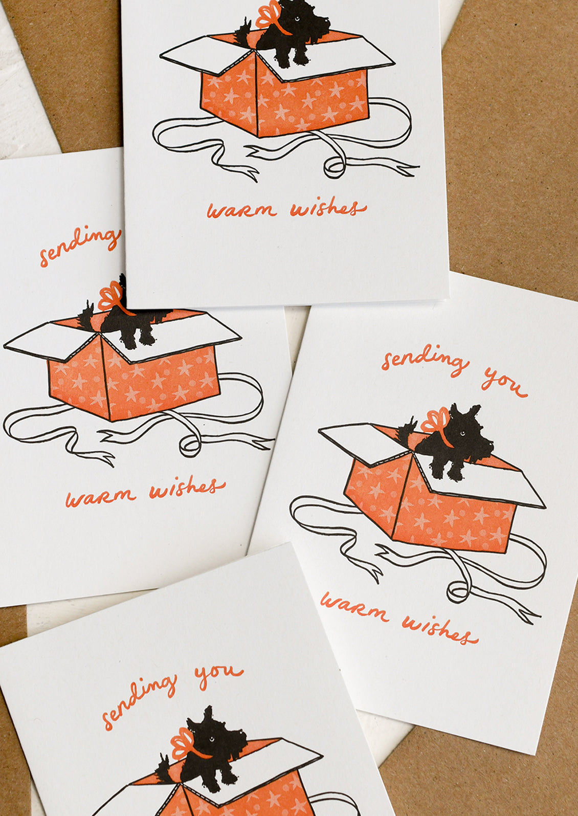 A greeting card with image of black Scottie dog jumping out of gift box, text reads "Sending you warm wishes".