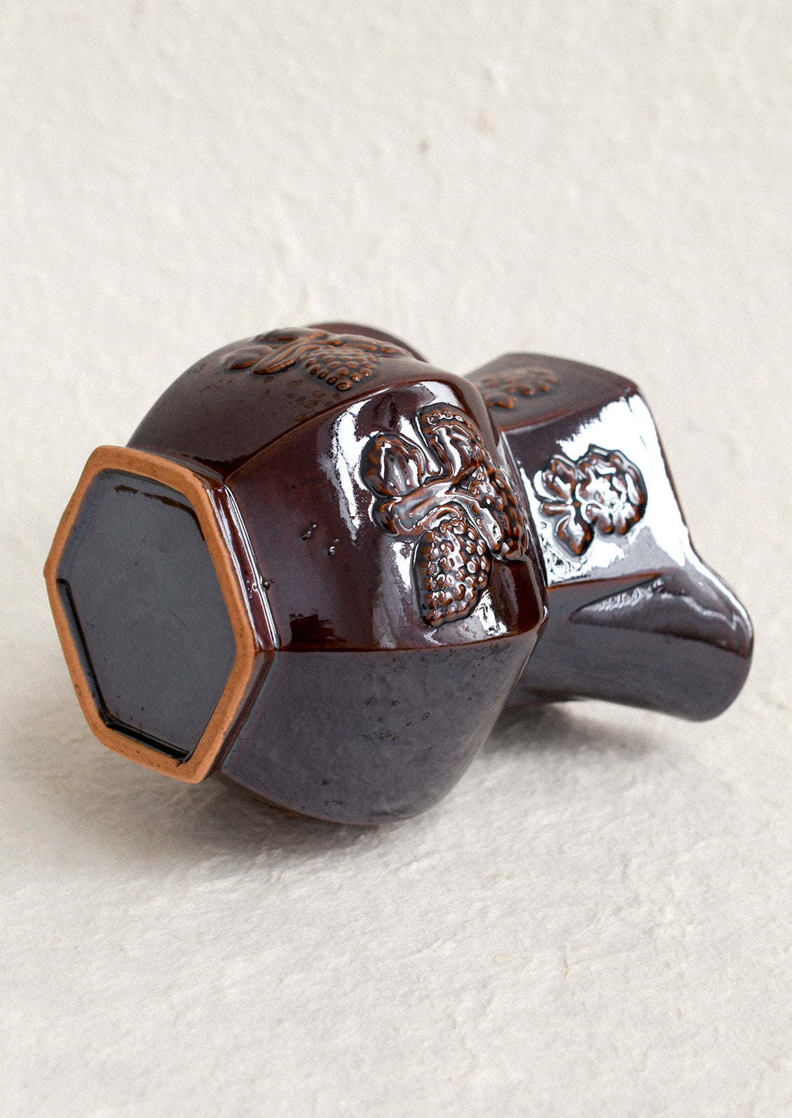 A dark brown pitcher with iridescent glaze and embossed floral pattern.