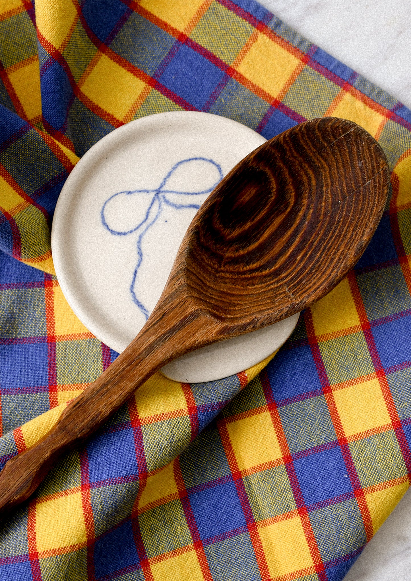 Wooden spoon on a white plate with a blue design on a colorful checkered fabric background