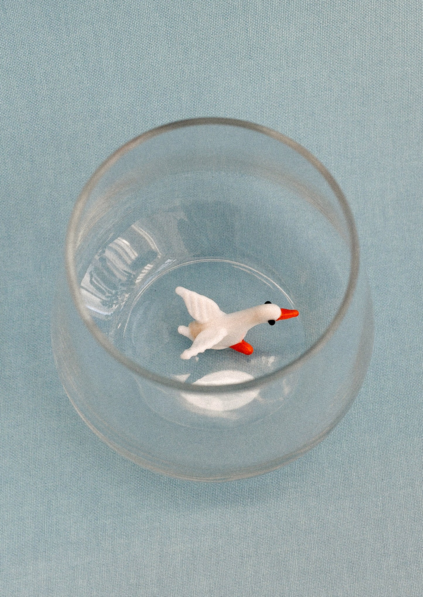 Clear glass tumbler with a small duck figure on a light blue background