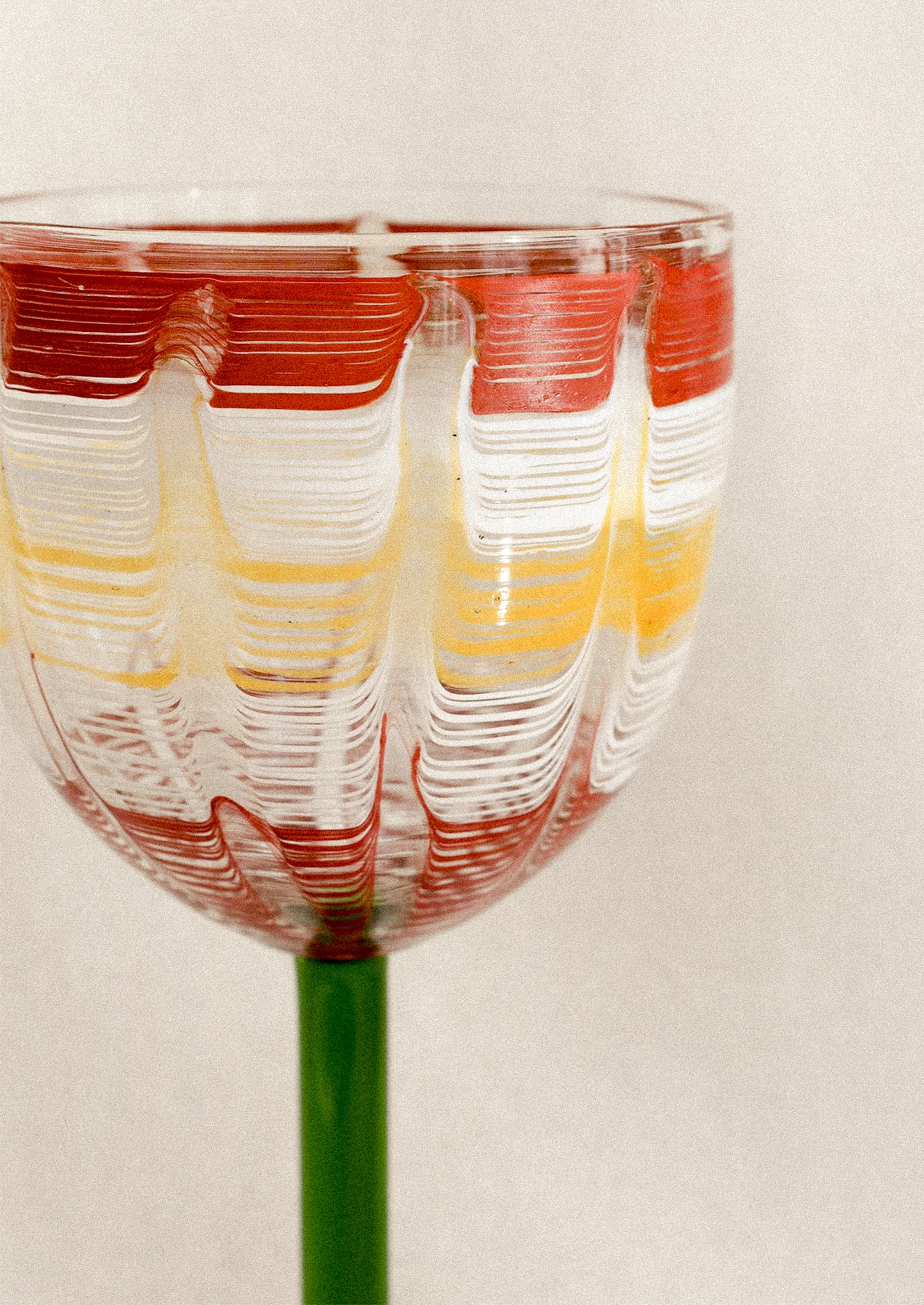 A wine glass with green stem and hand painted cup with abstract line pattern.