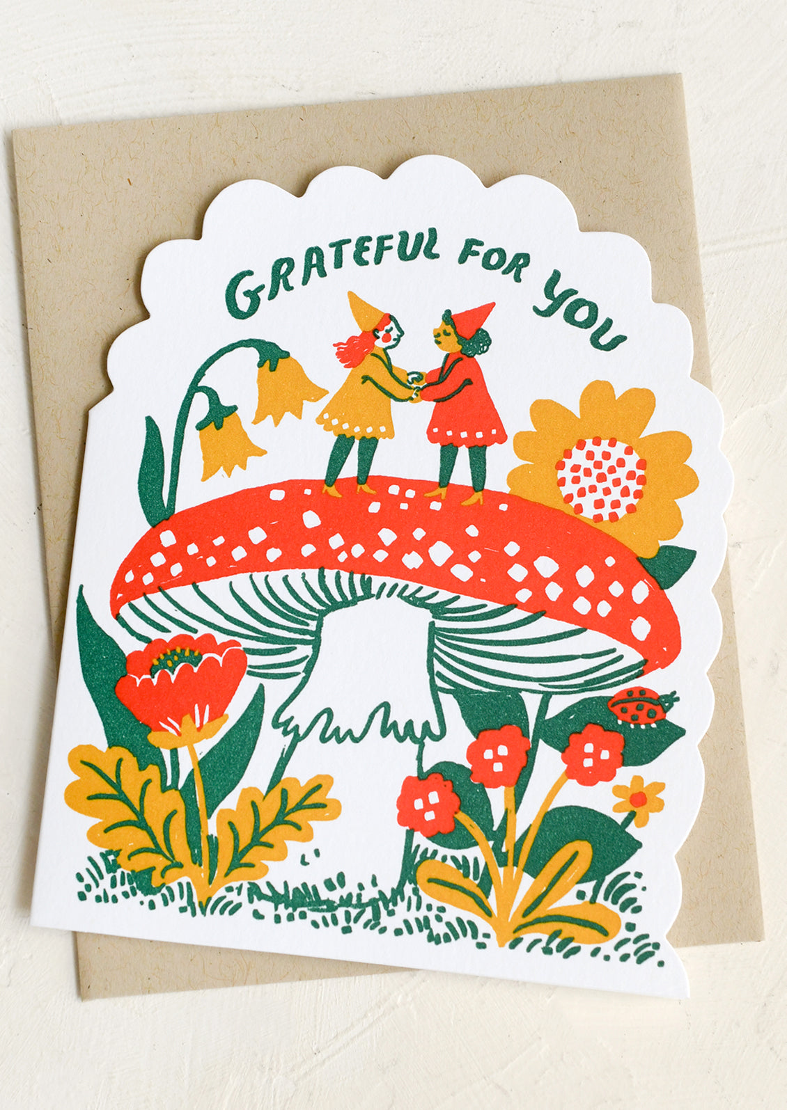 Greeting card with two gnomes holding hands under a mushroom, surrounded by flowers and text 'Grateful for you'.