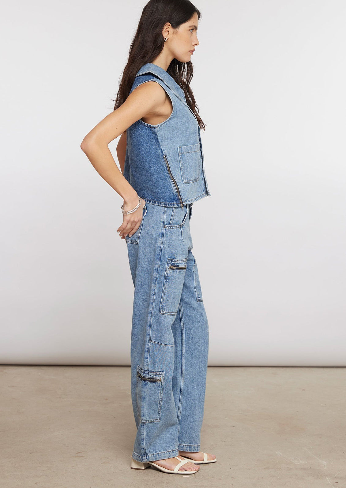 A person wearing light wash jeans with zip details on pockets.