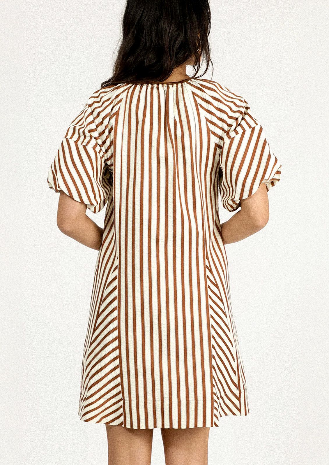 A person wearing a short dress in brown and cream vertical stripe pattern.