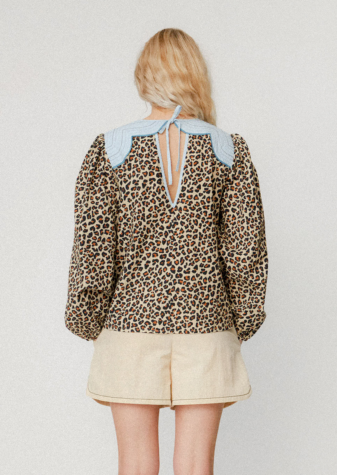 A woman wearing a leopard print blouse with light blue contrast yoke detail.
