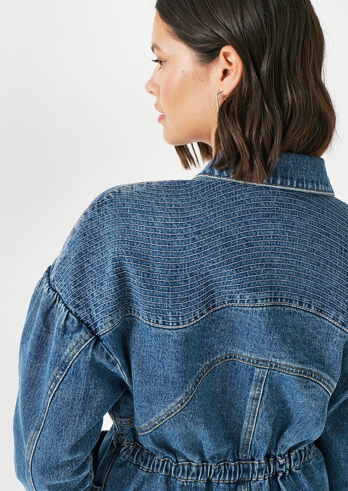 A woman wearing a denim jacket with decorative stitching and ruched shoulder detail.