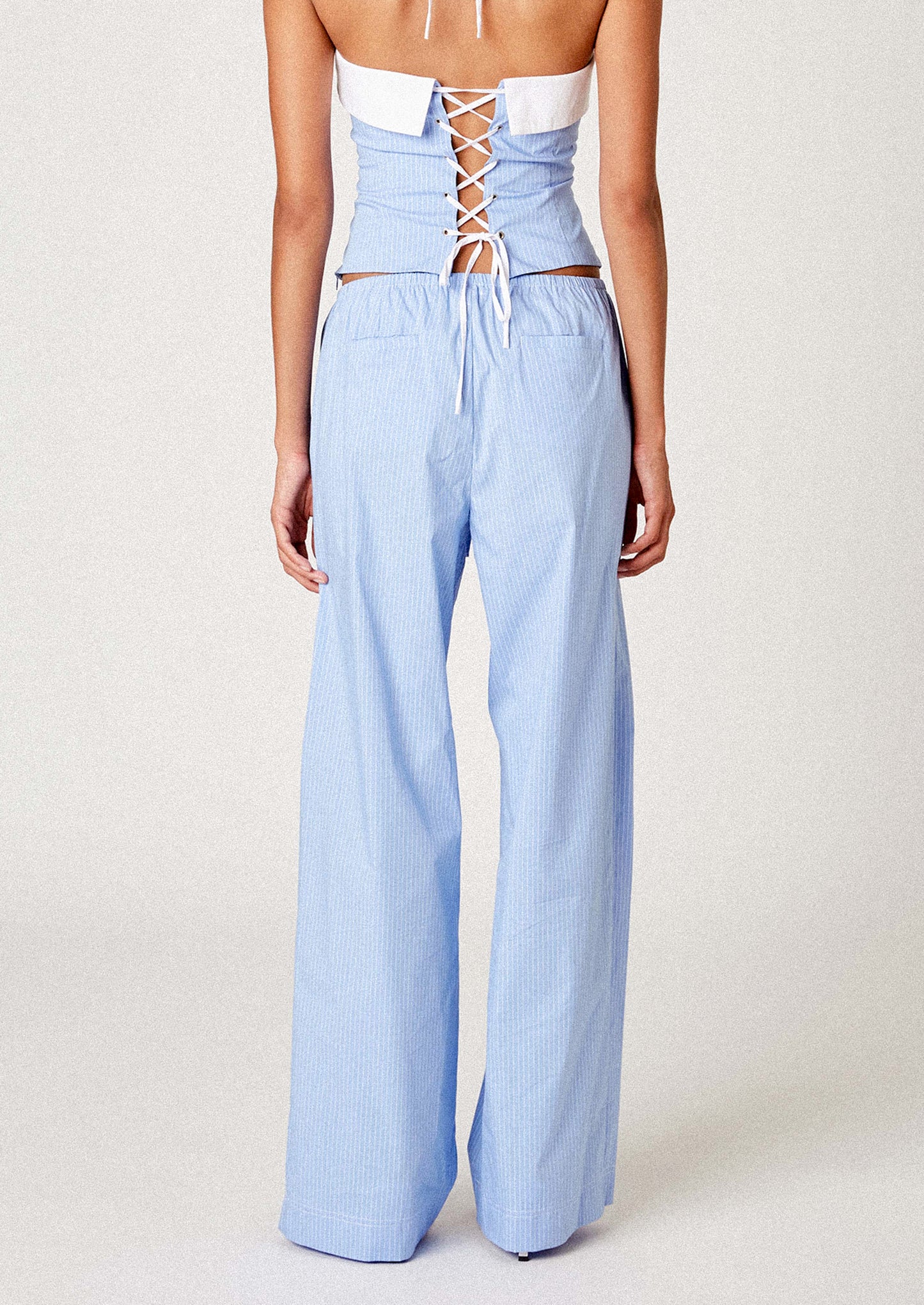 A person wearing a pair of pajama-inspired pants in blue with white pinstripe.