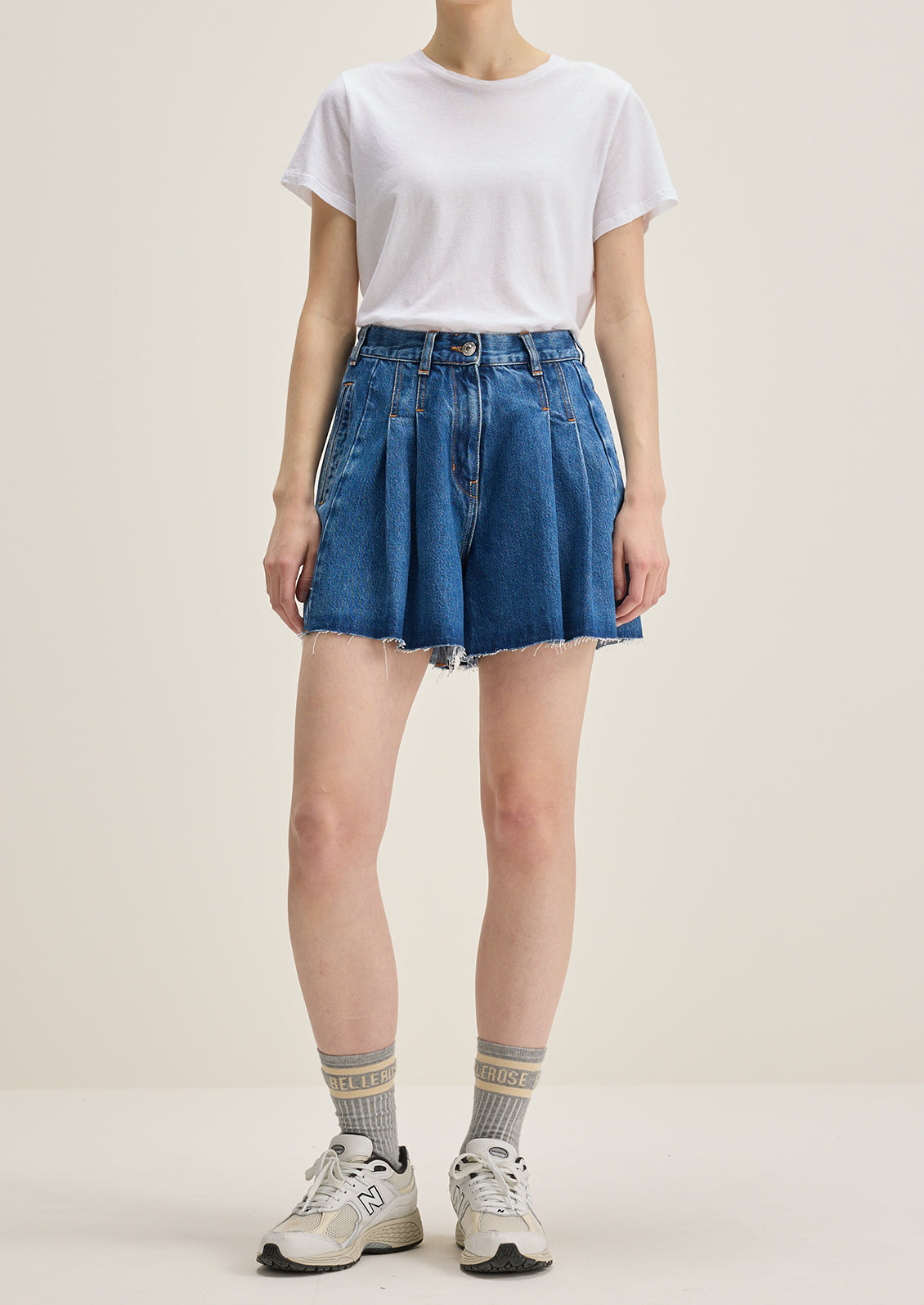 A person wearing a pair of pleated denim shorts in true medium blue wash.