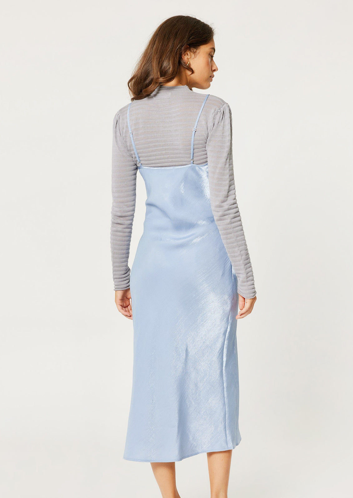 A woman wearing a periwinkle color sleeveless satin dress with empire silhouette.