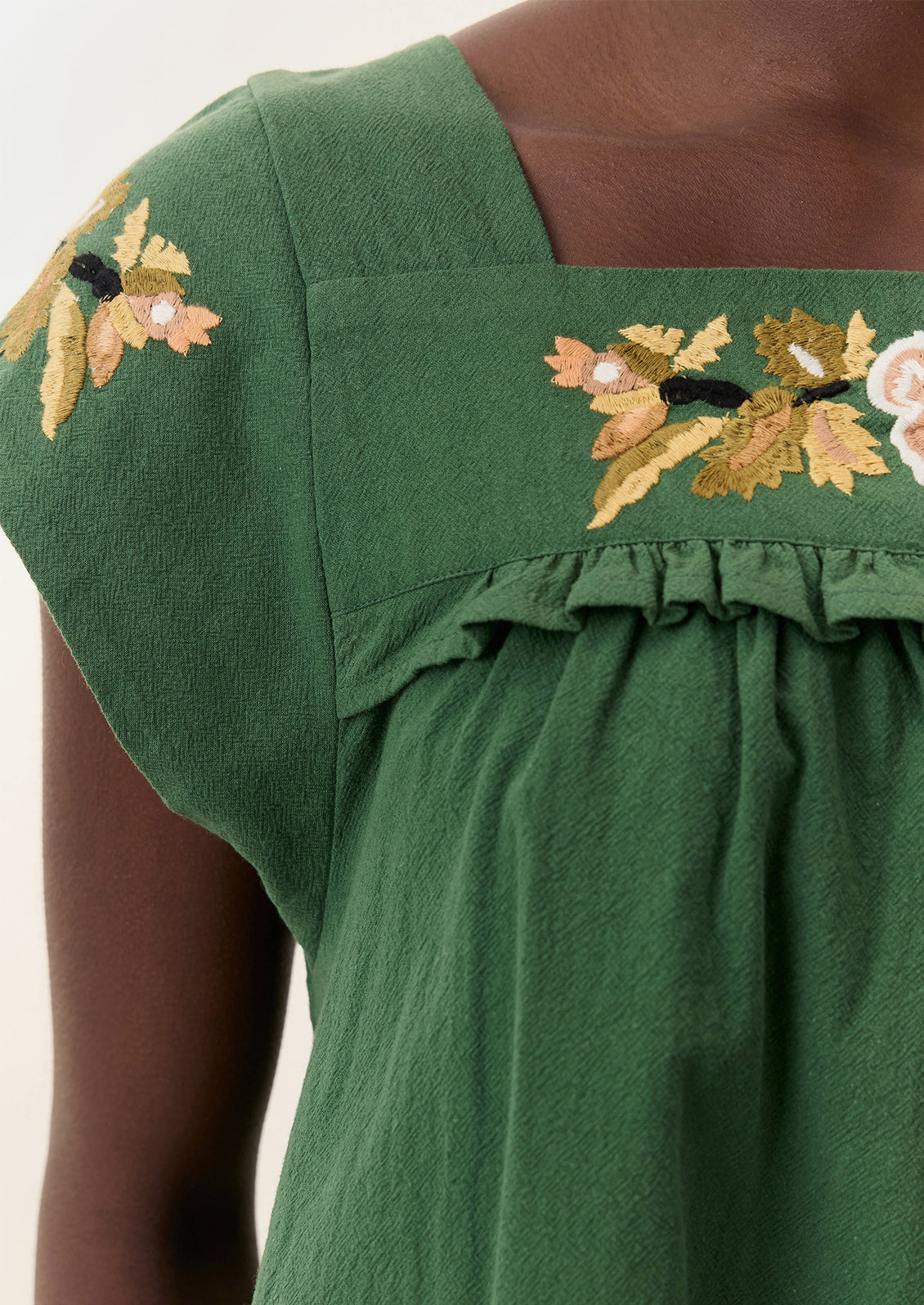 A person wearing a short green dress with yellow floral embroidery.