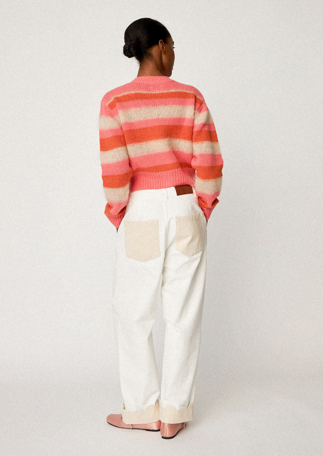 A woman wearing a button front cardigan sweater in pink, orange and ivory stripes.