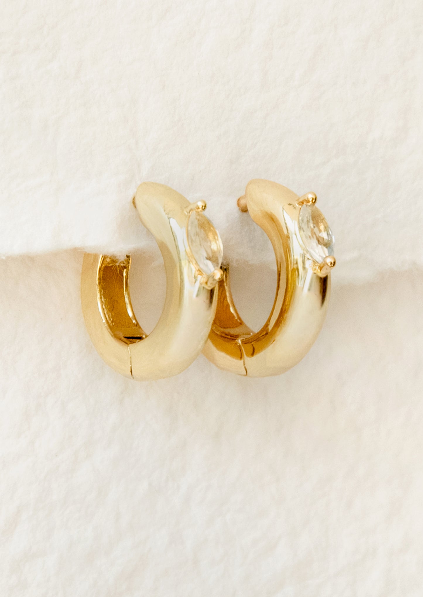 Gold hoop earrings with clear gemstones on a beige background