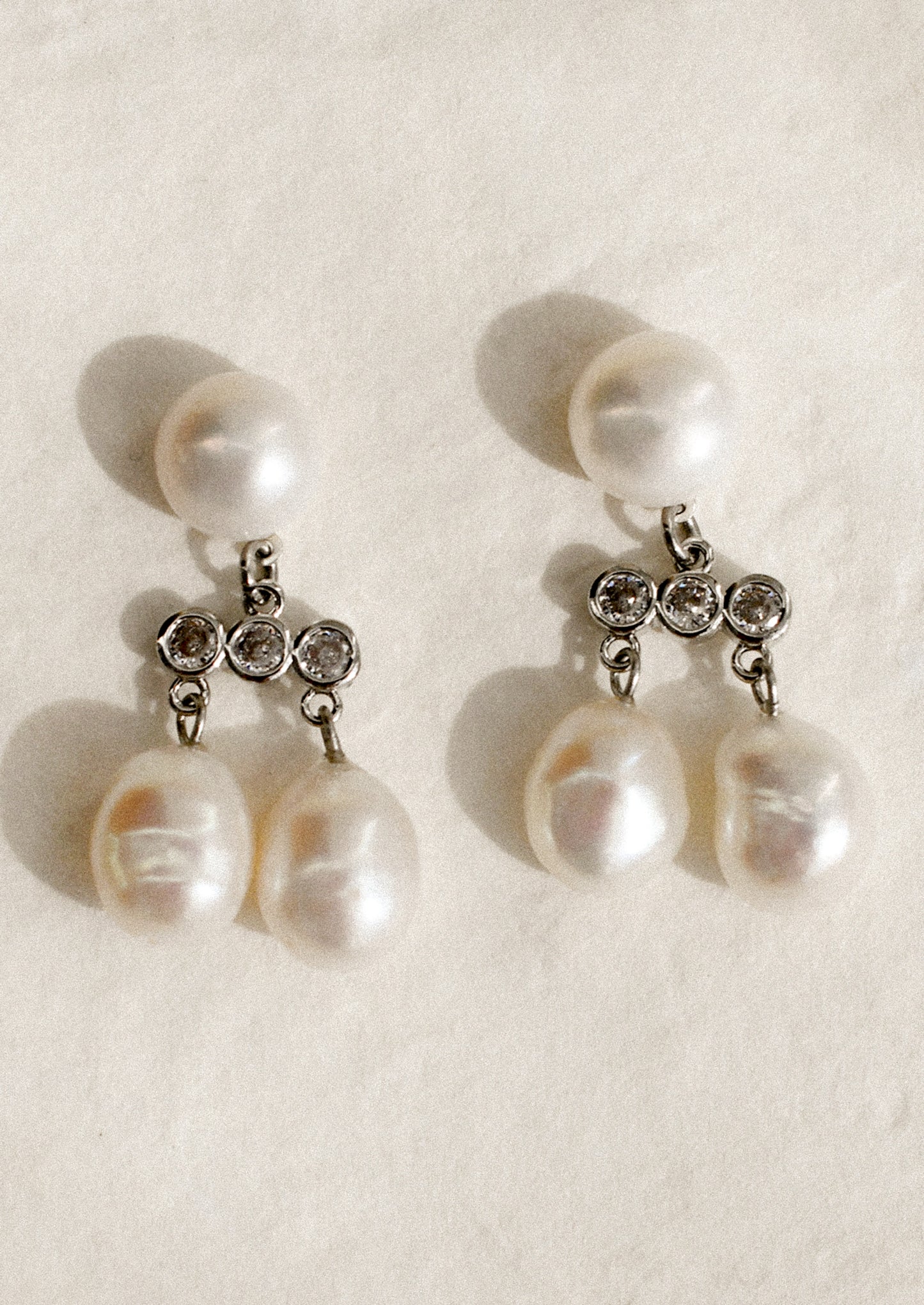A pair of stacked pearl drop earrings with triple crystal bar at center, in silver.