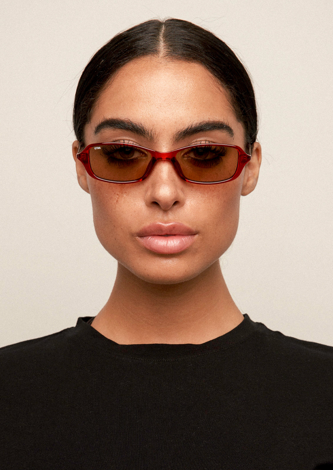 A woman wearing a pair of square sunglasses with a cherry brown frame and brown lenses.