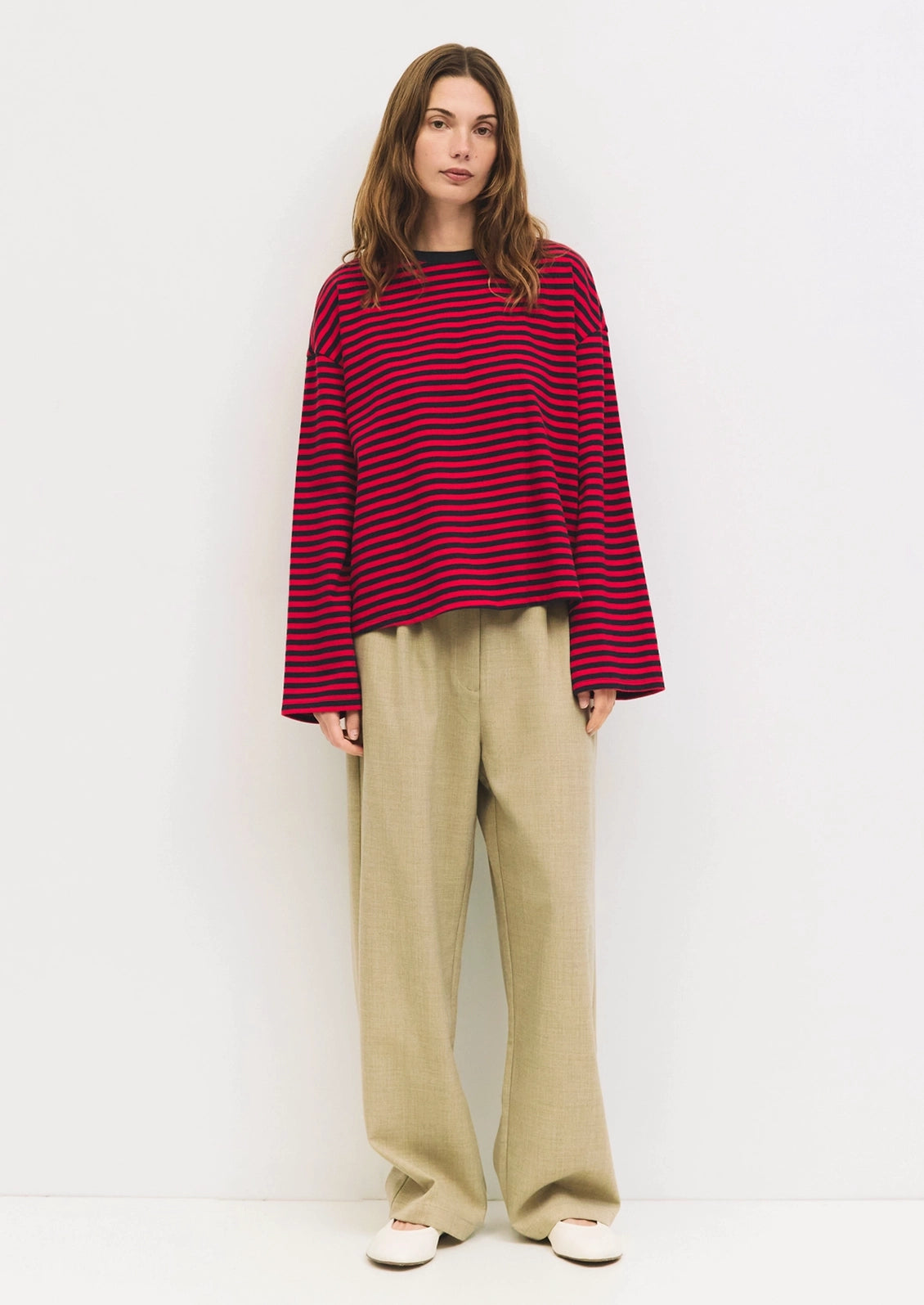 A person wearing an oversized long sleeve tee in red and navy stripes.