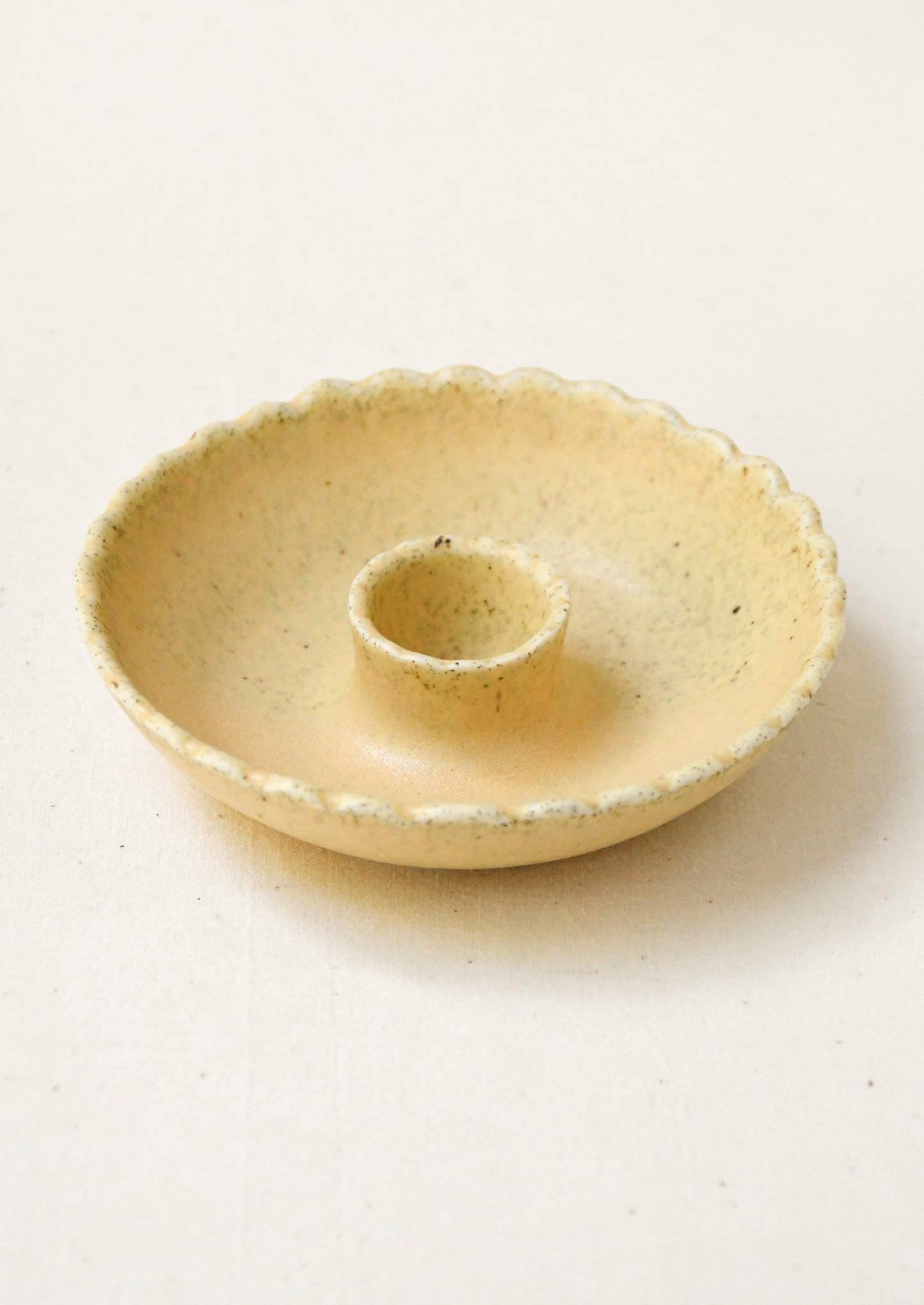 A porcelain candle holder with scalloped shape in butter yellow.