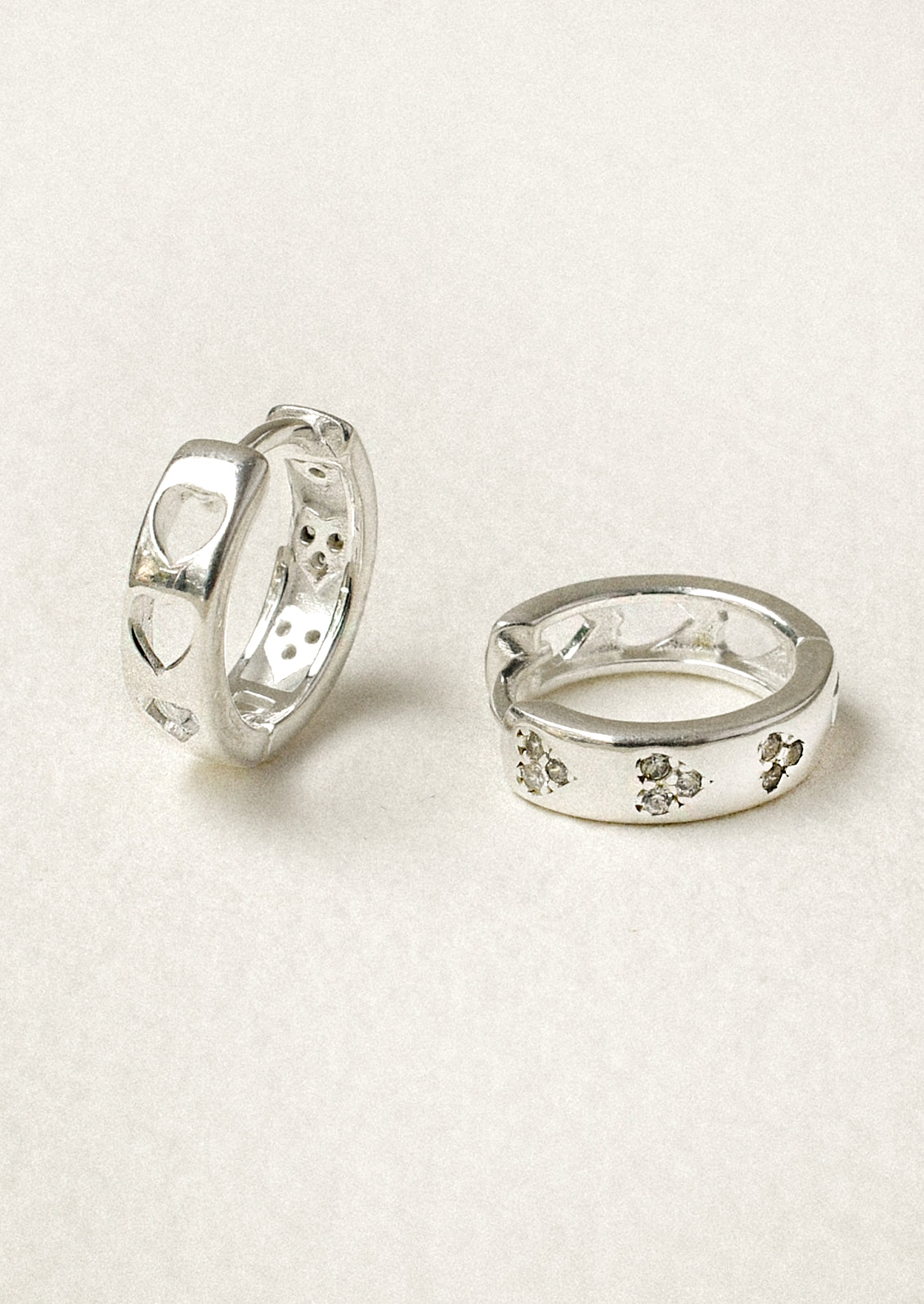 A pair of sterling silver huggie hoop earrings with heart-shaped holes on the back and crystal clusters on the front.