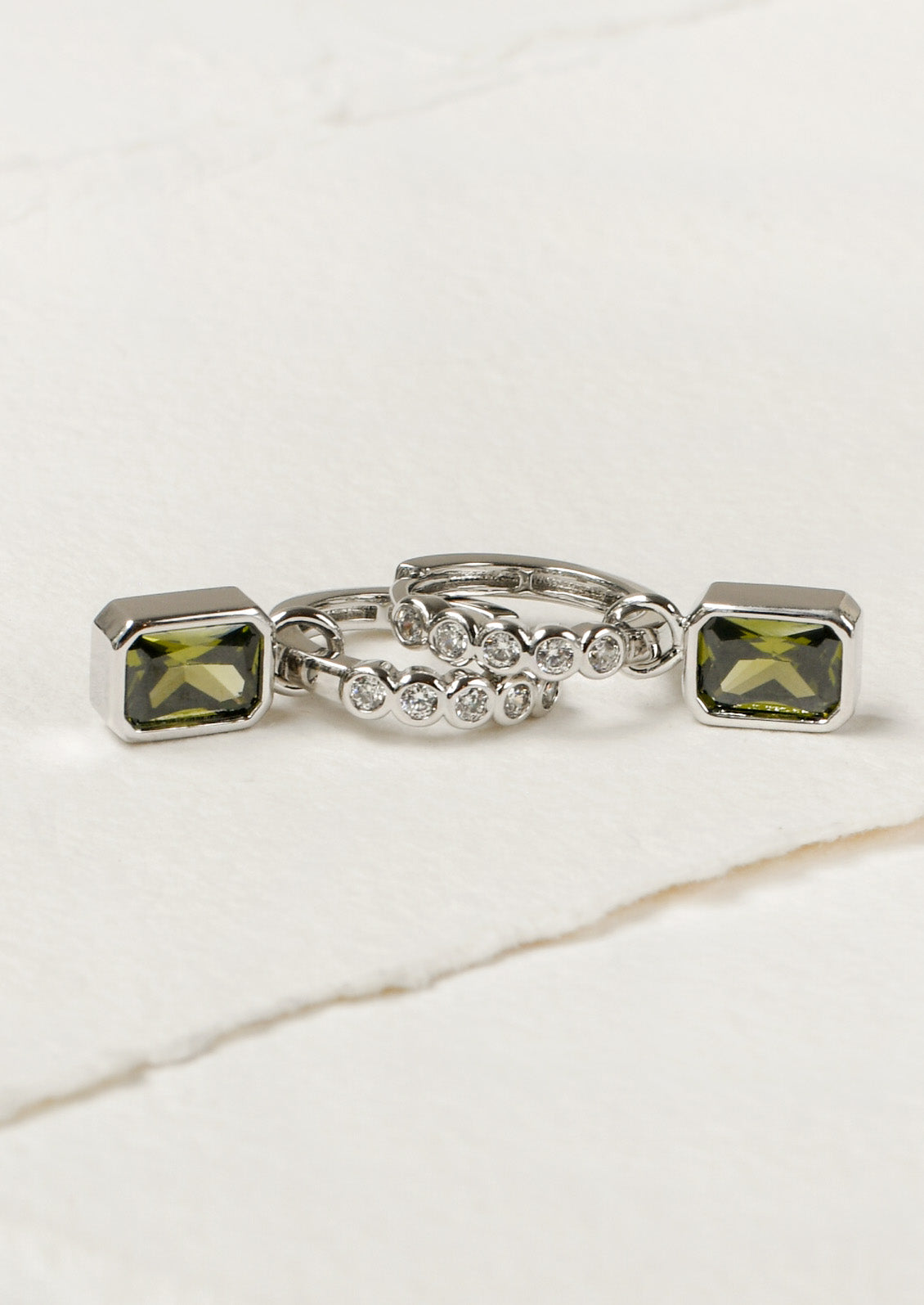 A pair of silver hoop earrings adorned with white crystals and dangling green gemstones.
