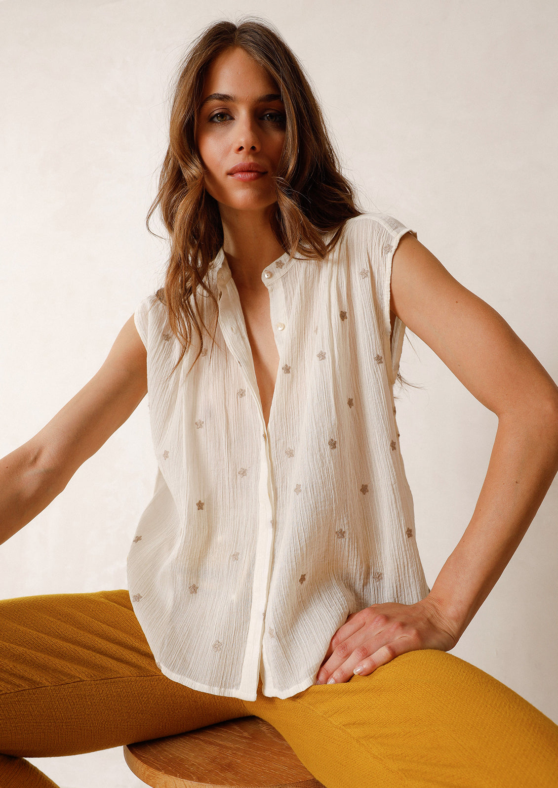 A woman in a white sleeveless top embroidered with grey stars.