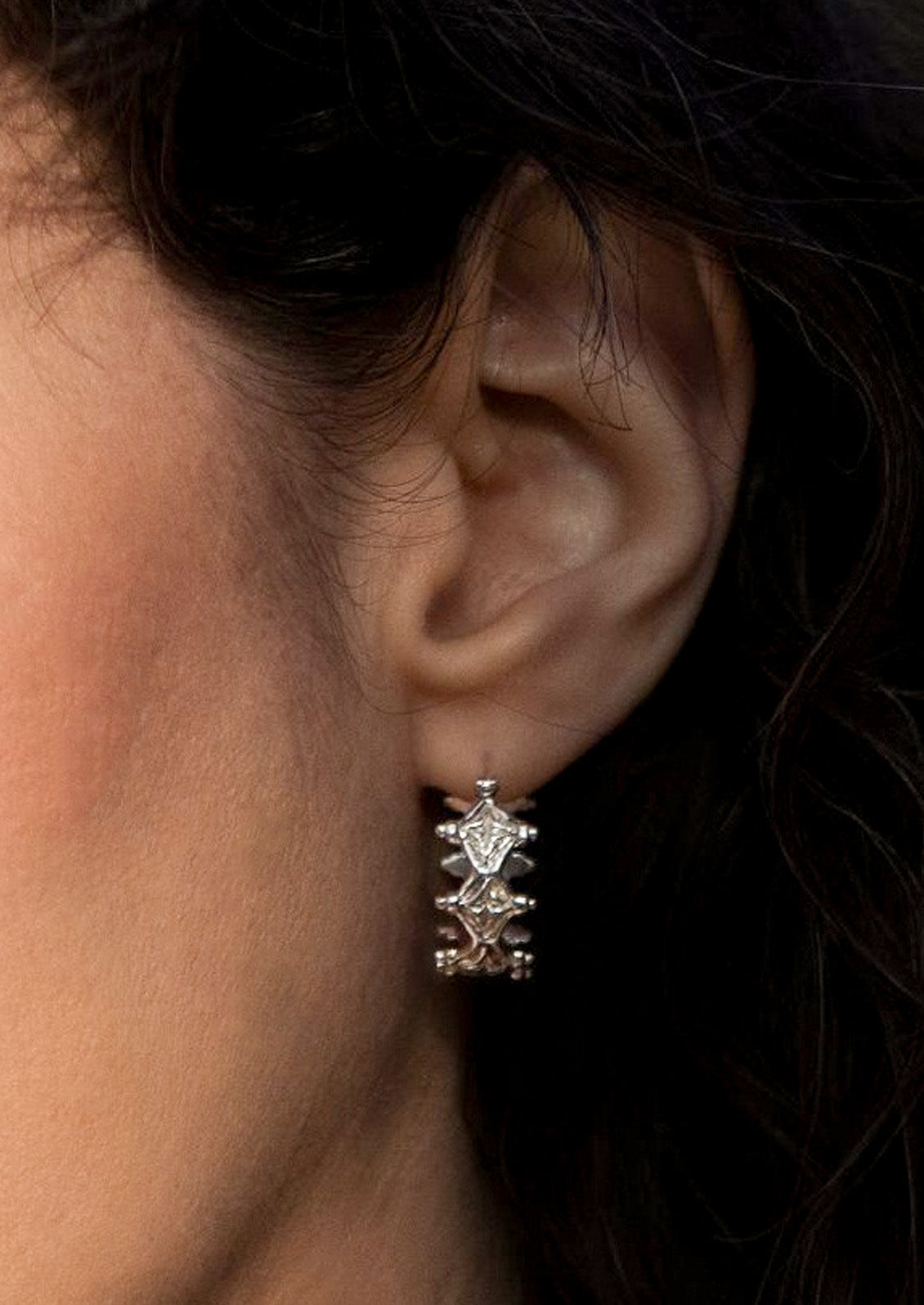 A woman wearing a sterling silver hoop earring with a unique diamond-like design.