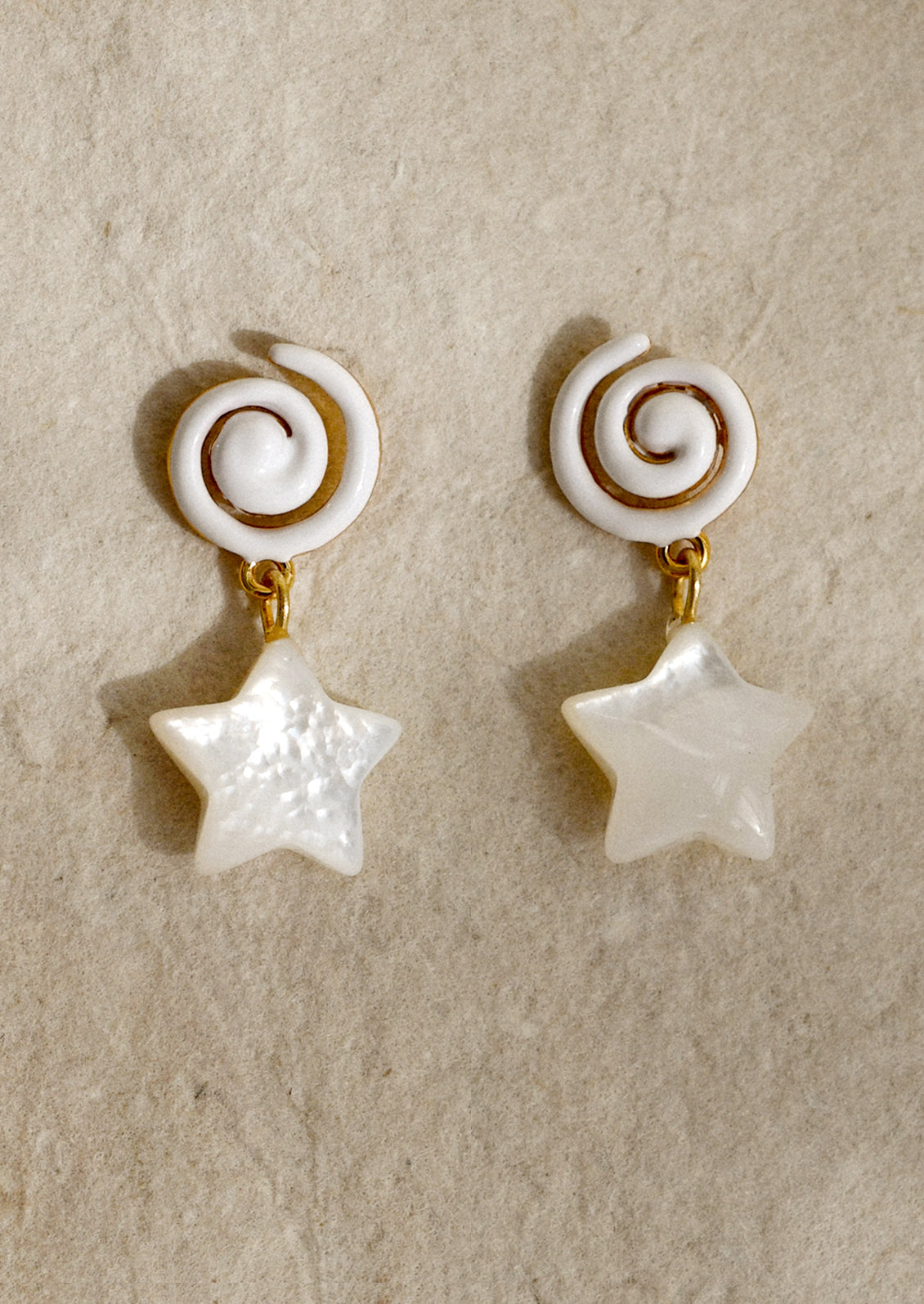 A pair of earrings with white swirl shaped enamel post and mother of pearl star charm.