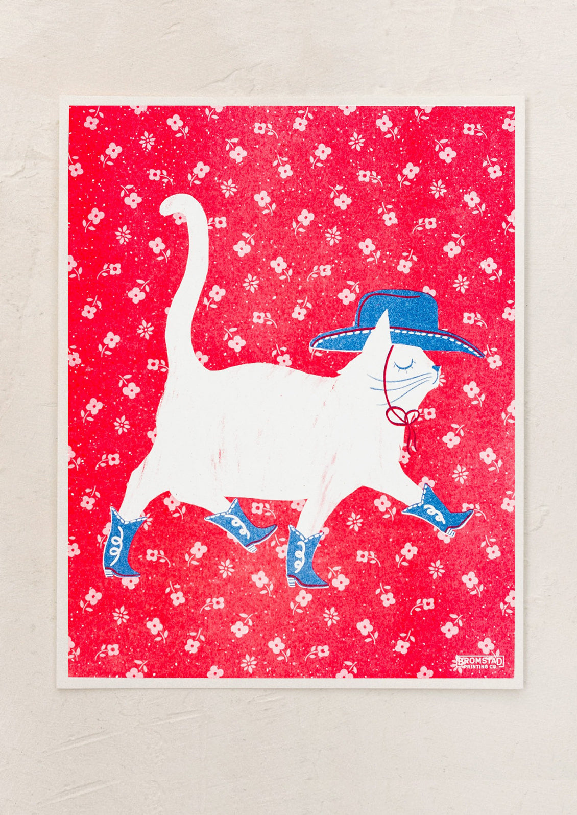 A risograph art print with a cat in cowboy hat and boots atop red flower background.