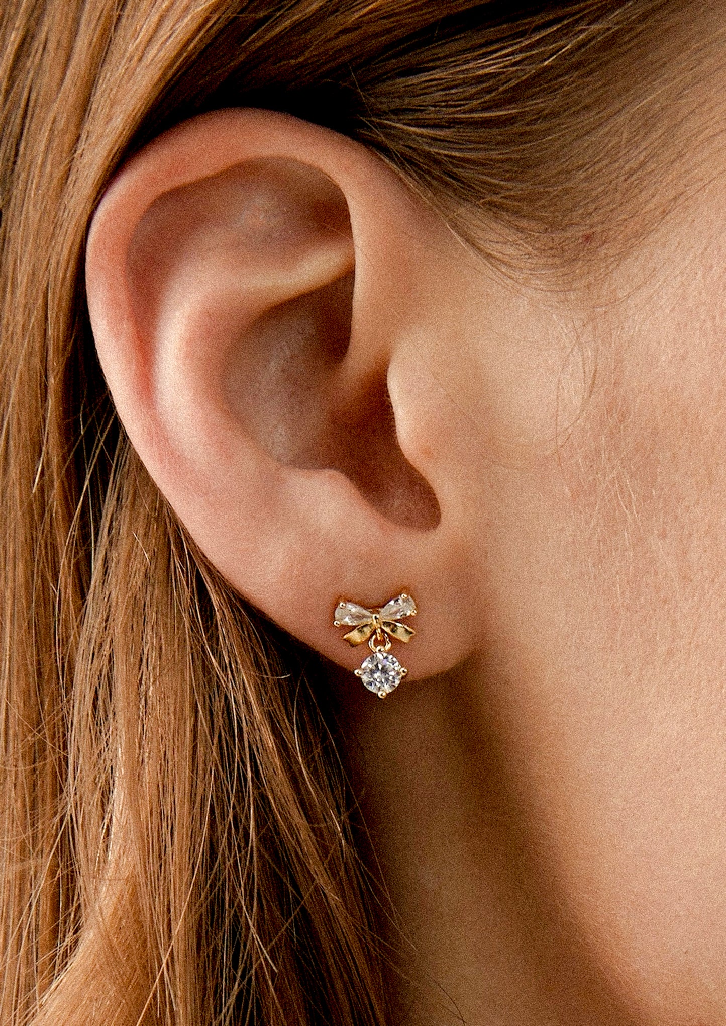 A person wearing a pair of bow shaped studs with crystal accents.
