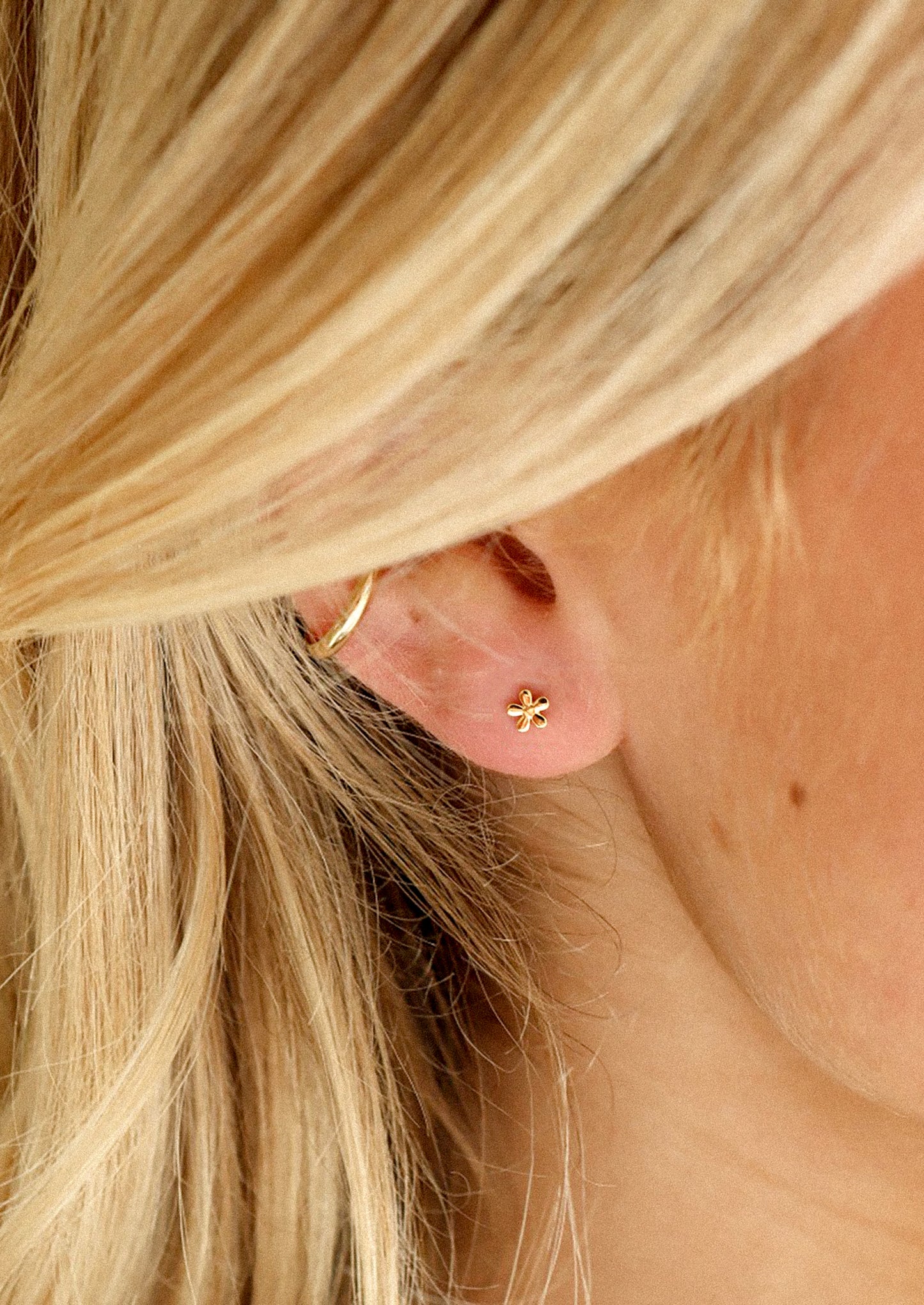 Close-up of a person wearing a gold earring with a flower design.