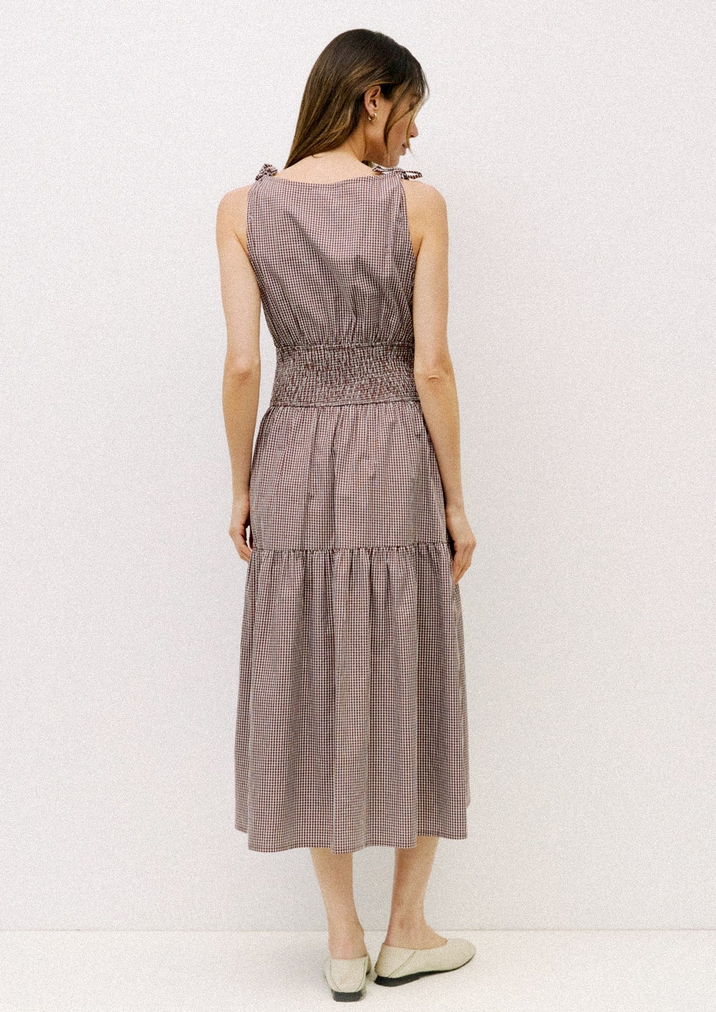 Woman wearing a sleeveless, tiered dress with a subtle pattern on a white background