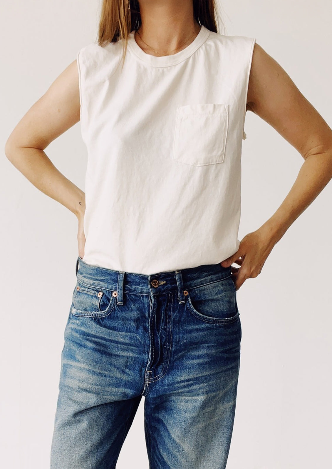 Person wearing a white sleeveless top and blue jeans on a plain background