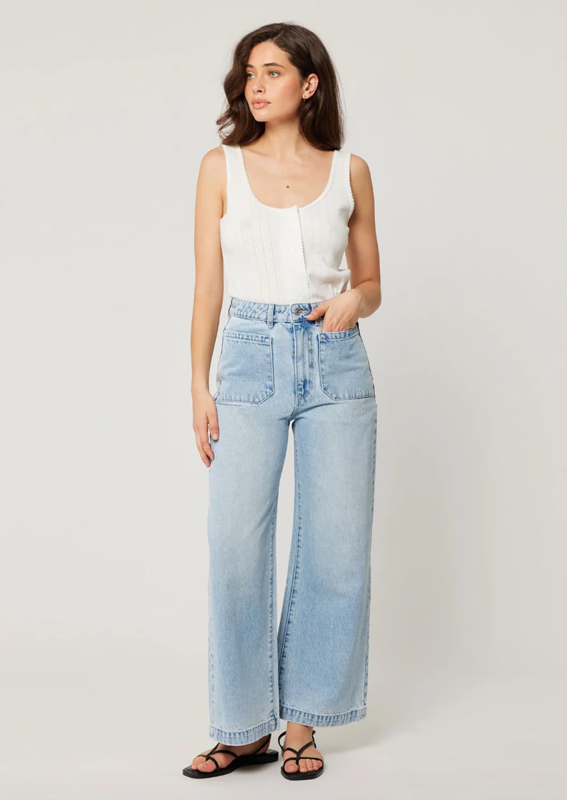 A person wearing a pair of light blue denim wide leg jeans with patch pockets at hips.