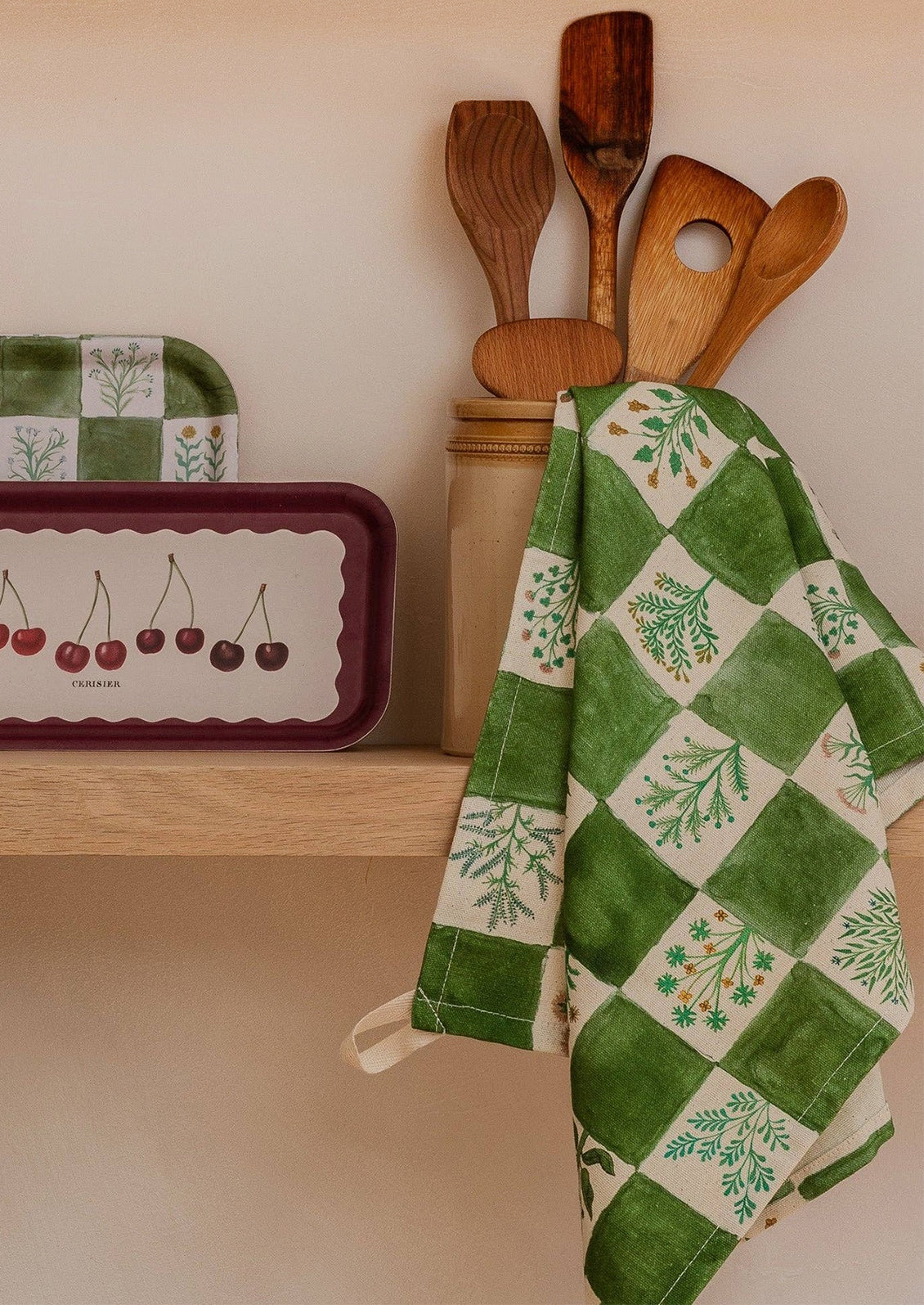Green and white checkered towel with floral patterns hanging on a wooden spoon holder against a beige wall.