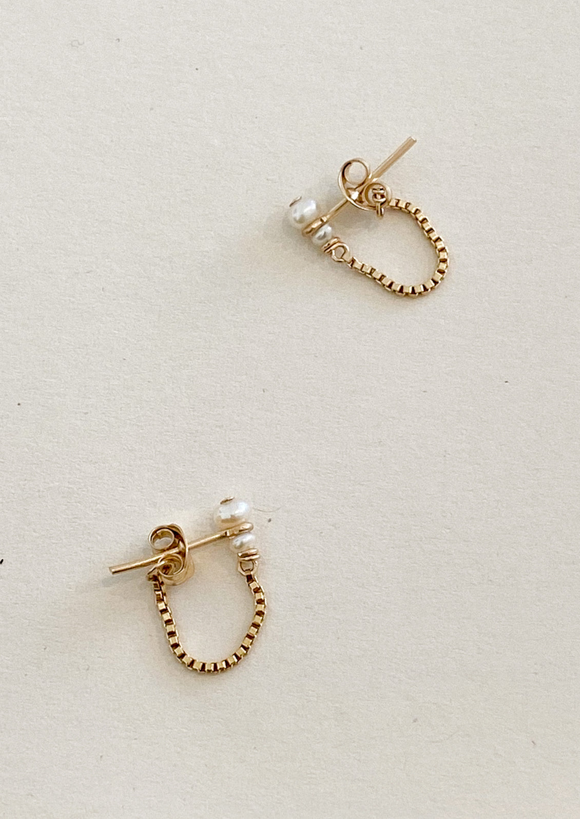 Gold hoop earrings with pearl accents on a light gray background