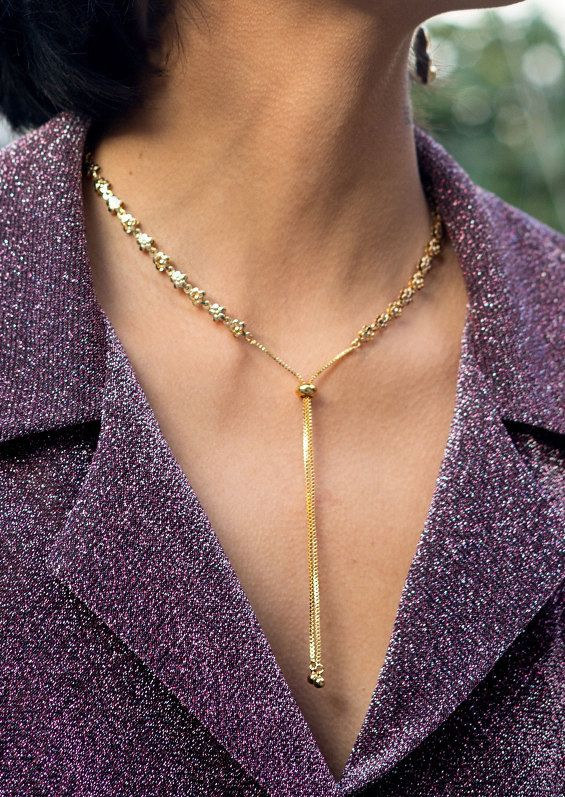 A lariat style necklace in gold with flower detail.