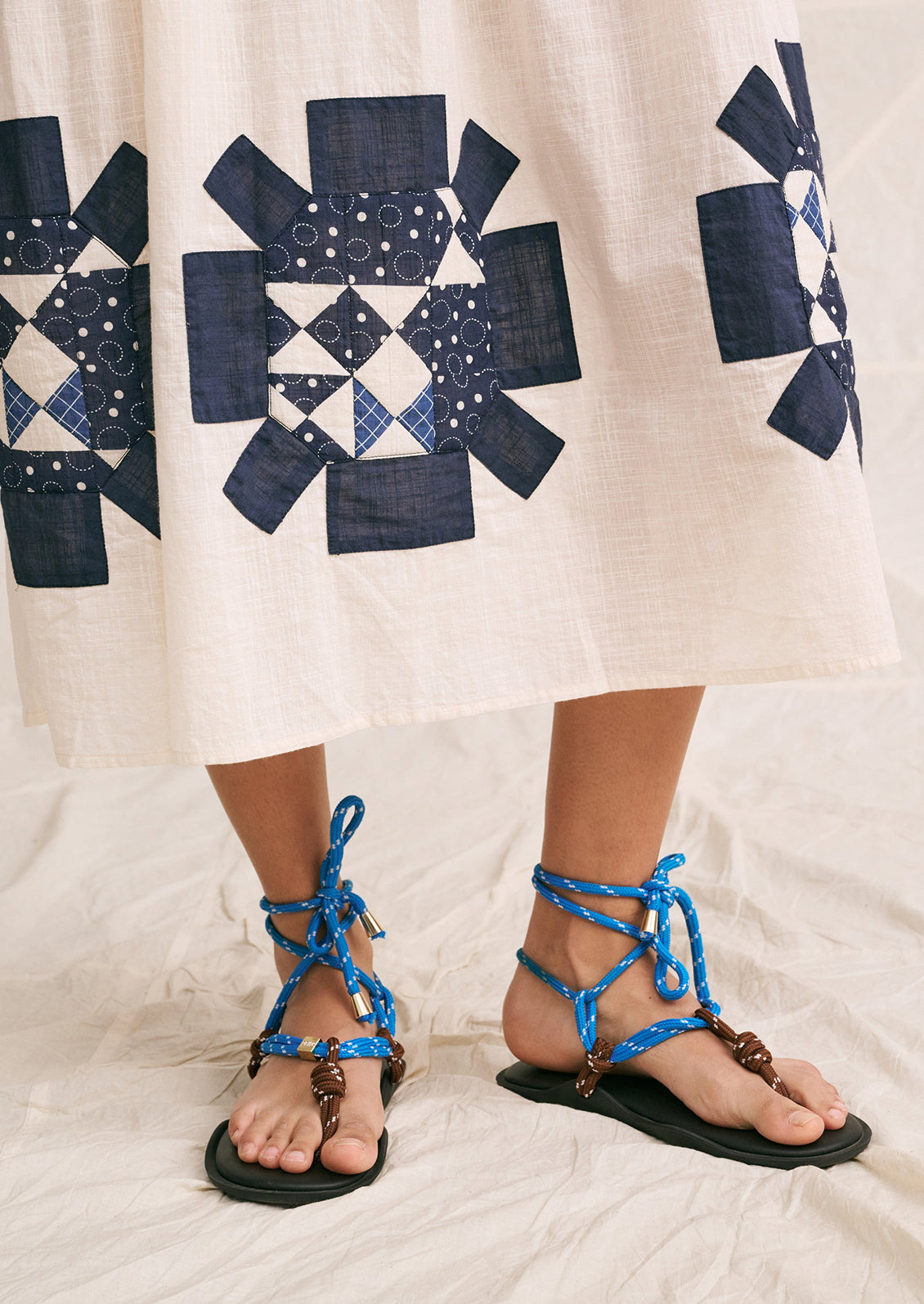 A woman wearing a long white sundress with indigo patchwork quilting details.