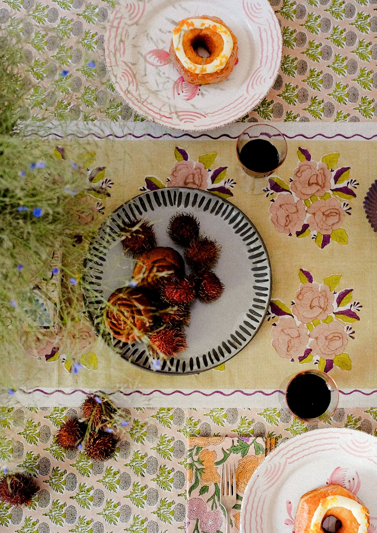 A linen table runner with pale yellow floral pattern and wavy purple border.