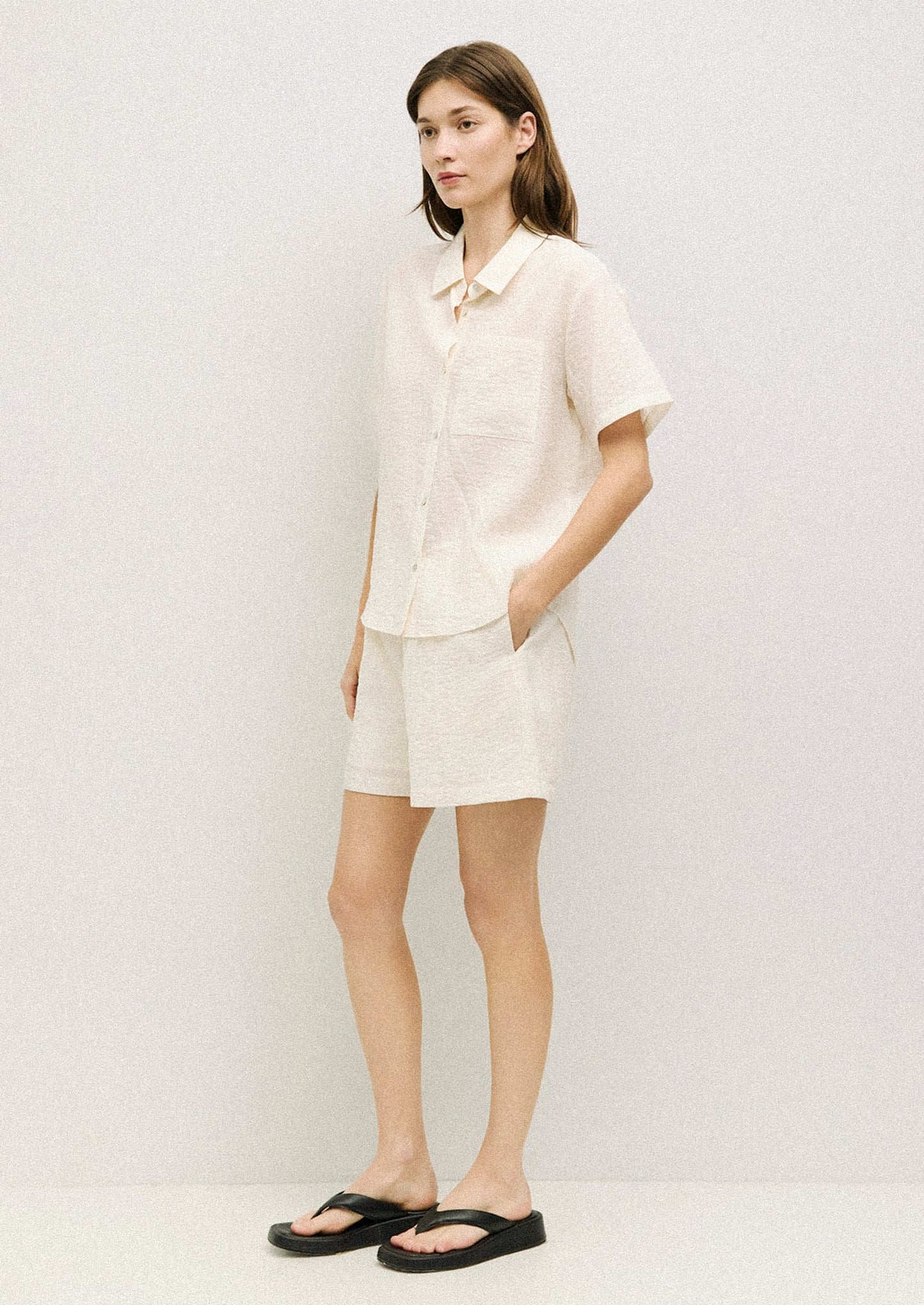 A woman wearing a short sleeve collared button front shirt in cream with soft wrinkled texture.
