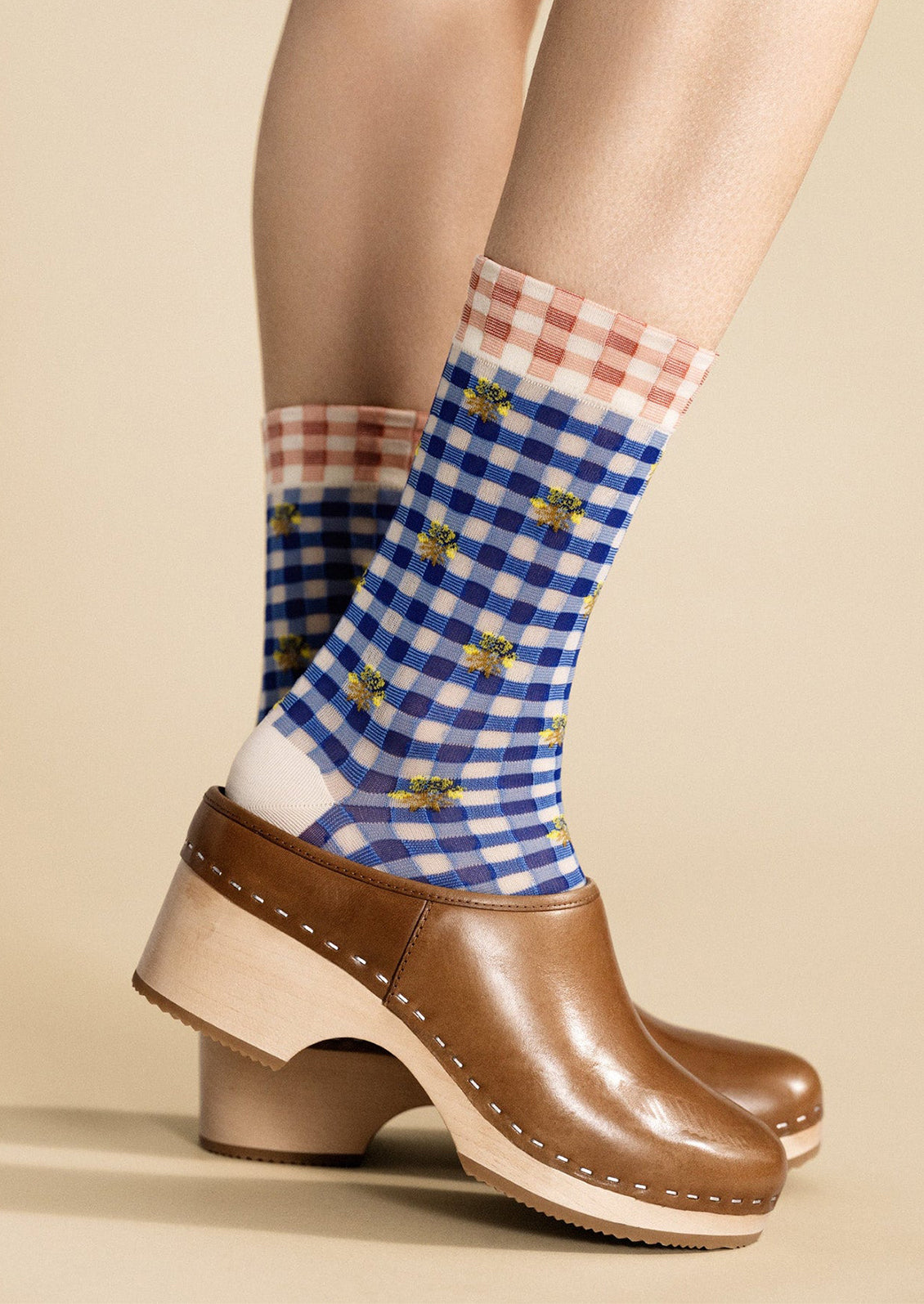 Checkered socks with a pattern of blue, red, and white worn with brown clogs on a beige background