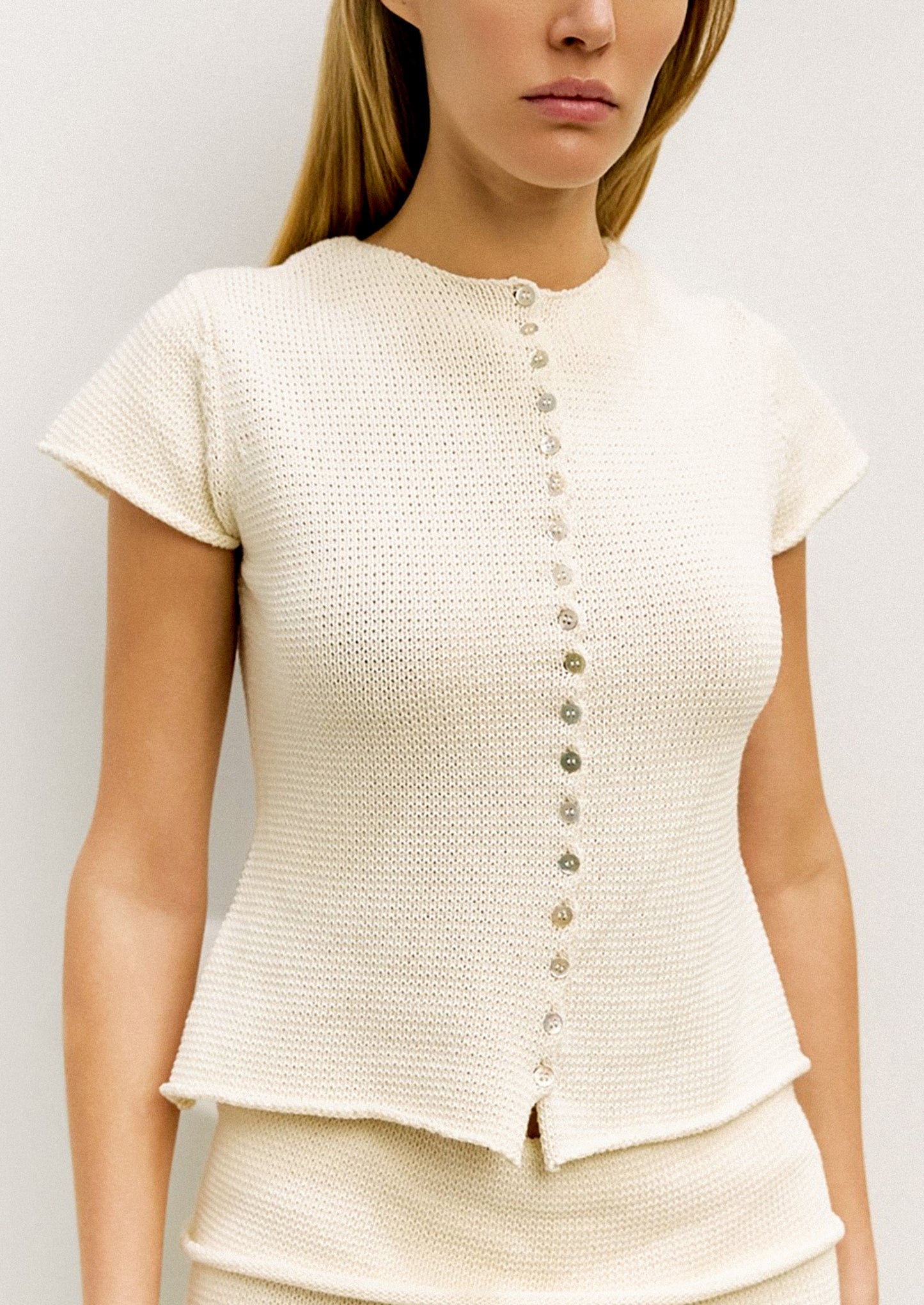 Woman wearing a cream-colored textured top with buttons on a plain background