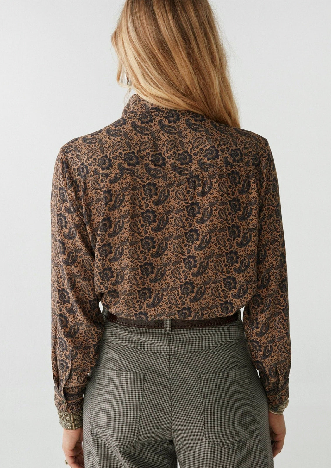 A woman wearing a paisley print blouse in brown and black.