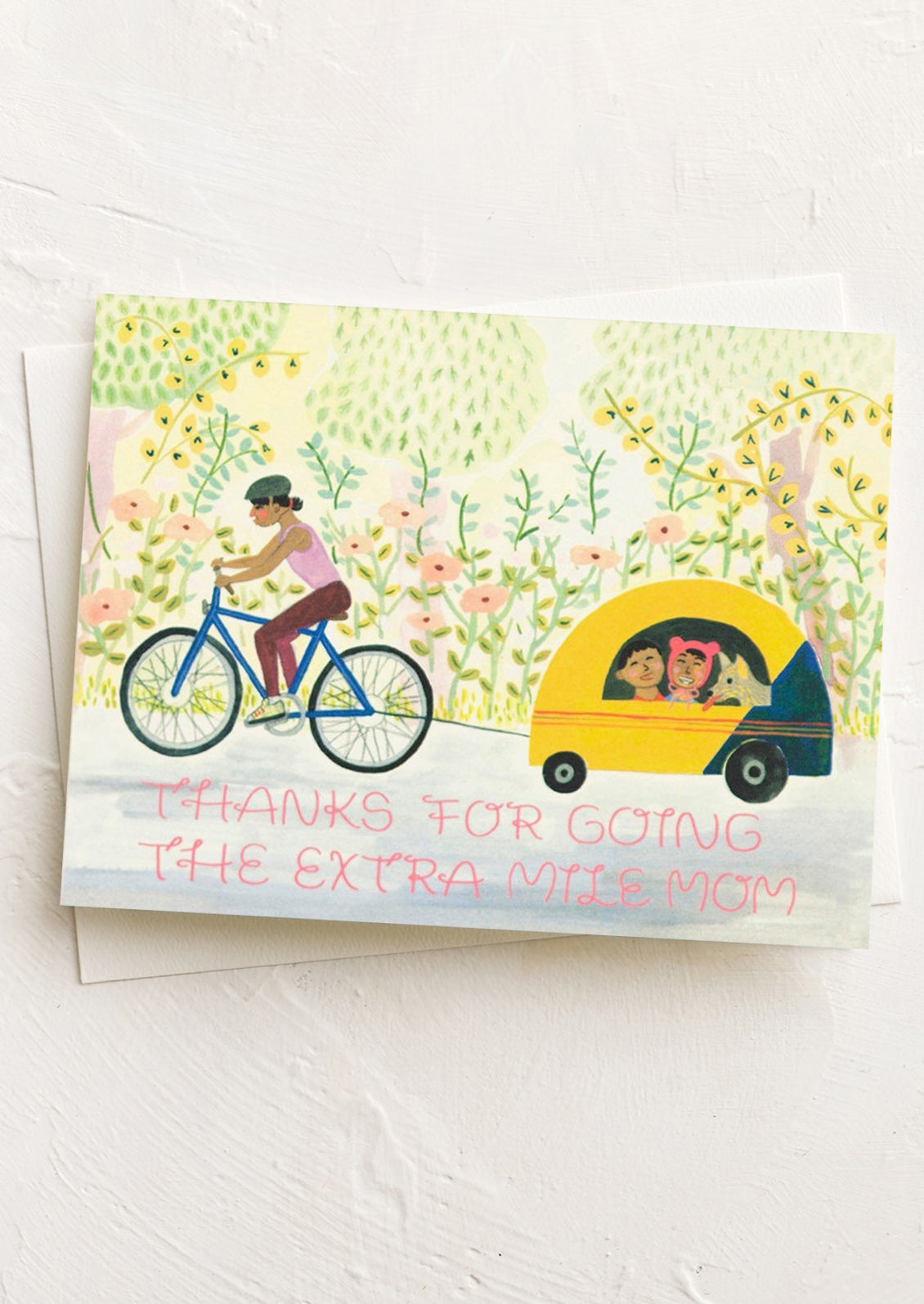 Greeting card with illustration of a woman on a bike and a child in a car, set against a floral background.